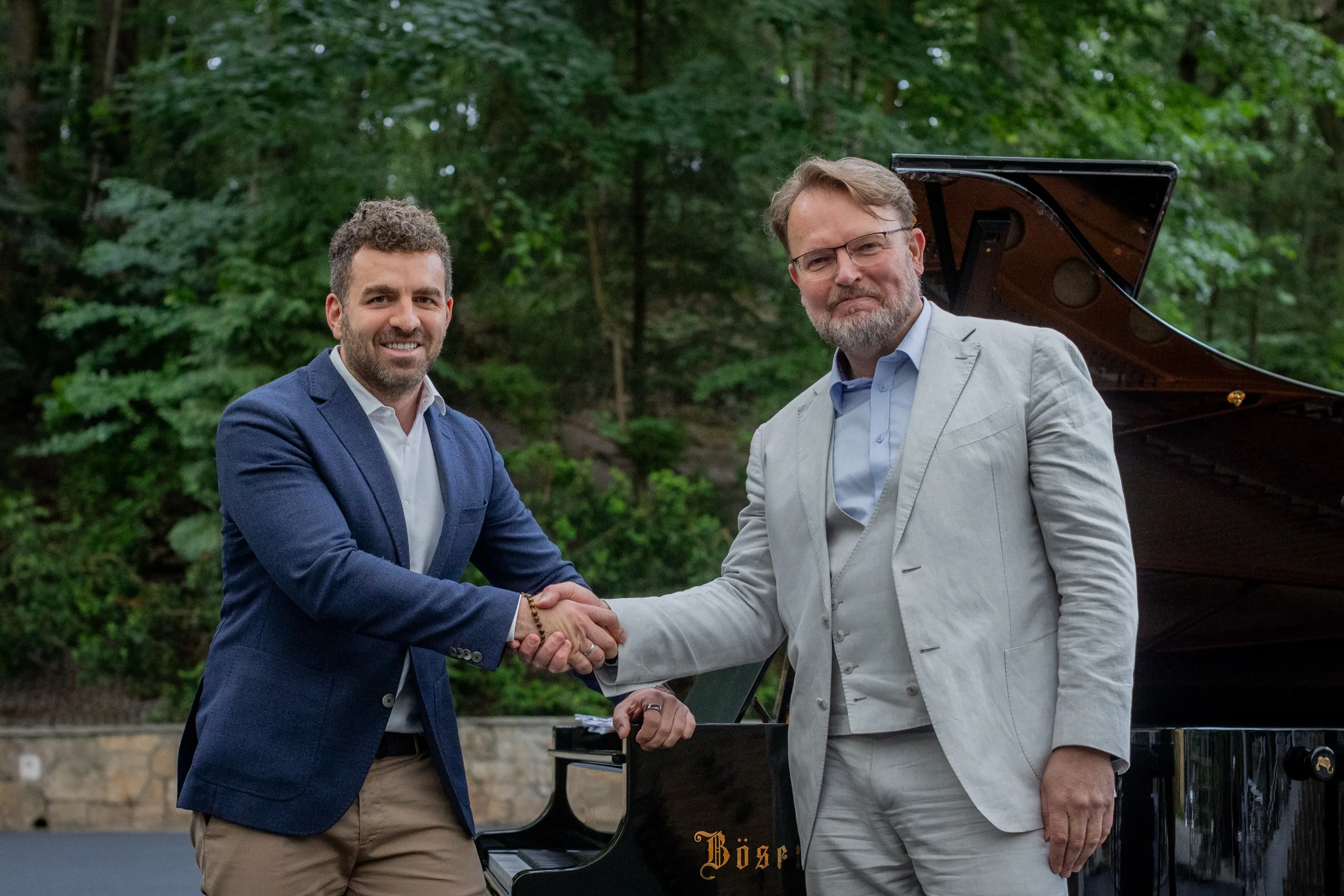Two men shaking hands beside a grand piano at the Baltic Opera Festival