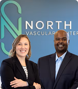 Two smiling professionals standing in front of North Vascular Center sign on blue wall.