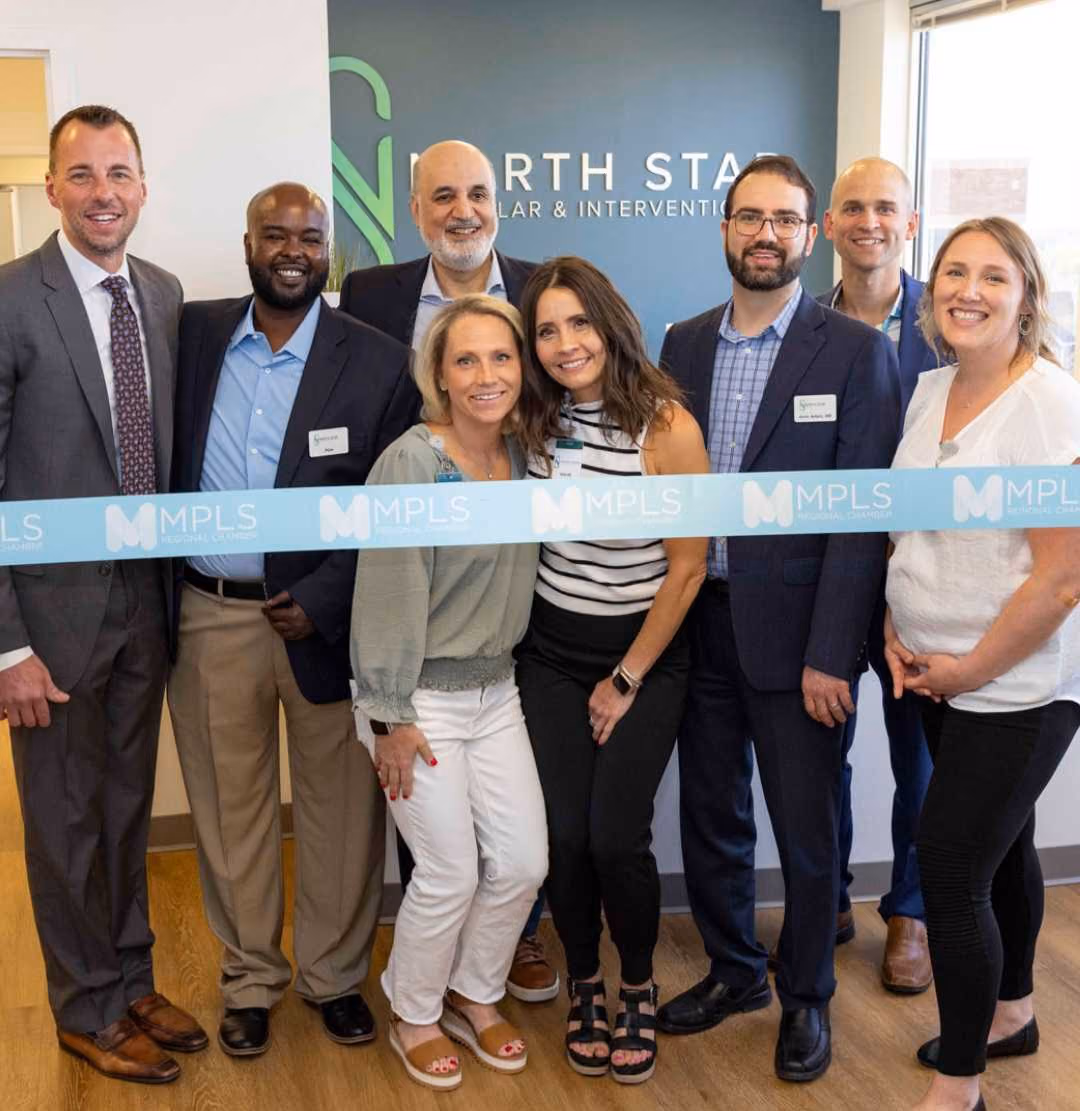 Eight people smiling and posing behind an MPLS Medical Dentistry ribbon for a ceremonial event.