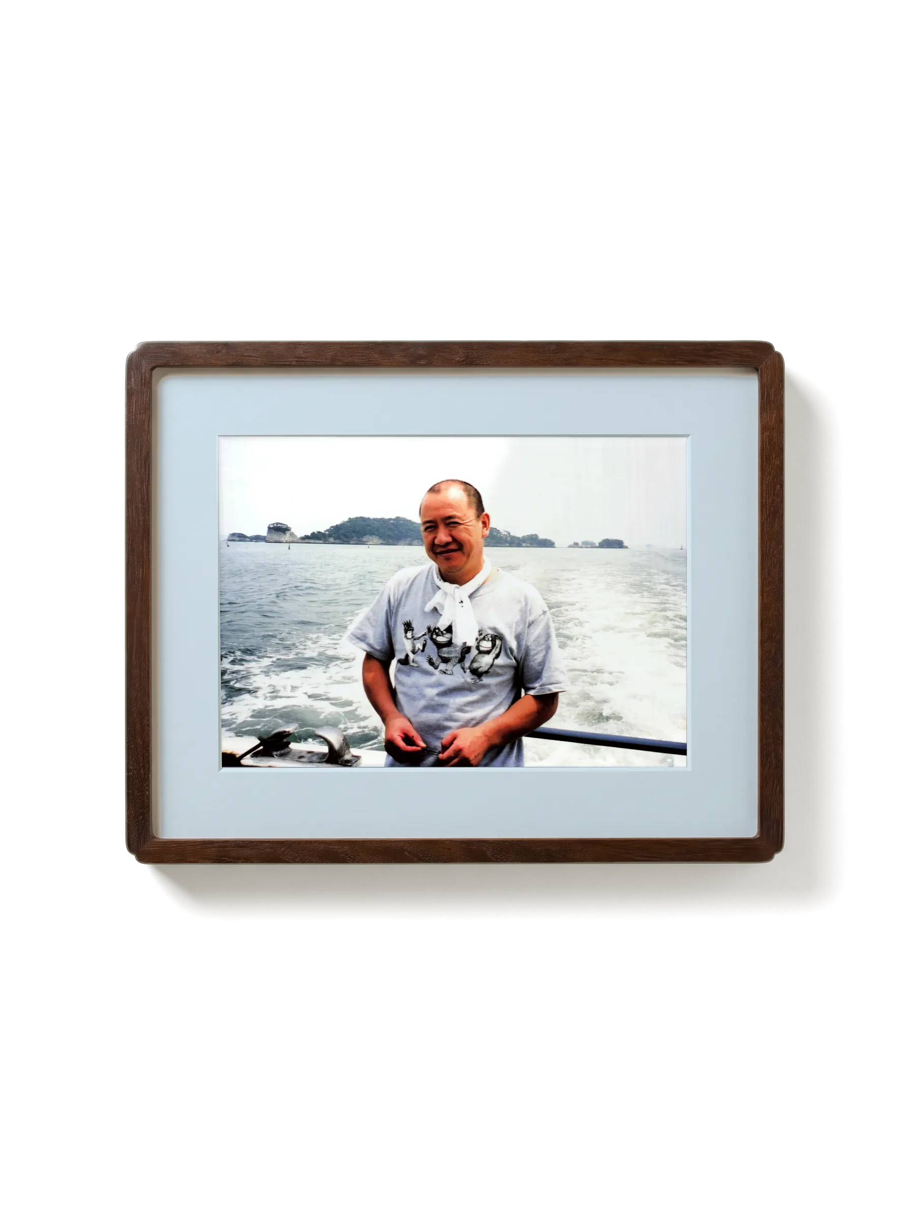 A photograph of Chef Masa on a boat, in a walnut frame with a pale mount
