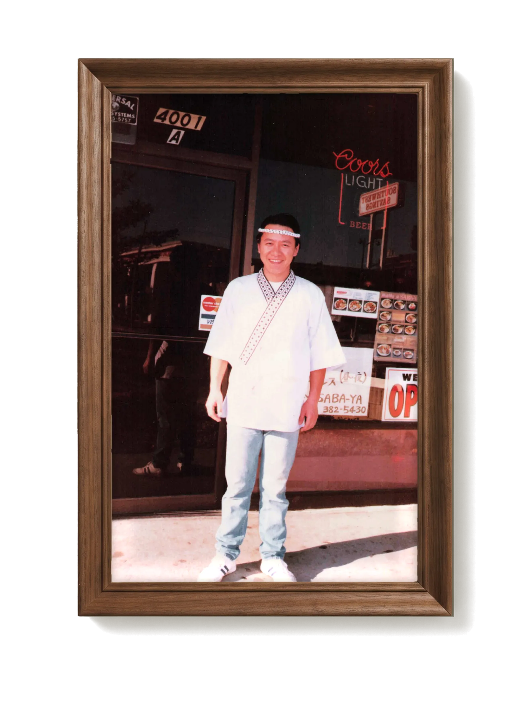 A vintage photograph of Chef Masa outside Saba-ya, in a dark walnut frame