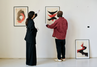 Two people hanging abstract artworks on a gallery wall