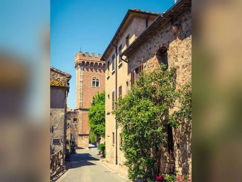 Via del borgo con casa in pietra, rampicante e torre in mattoni
