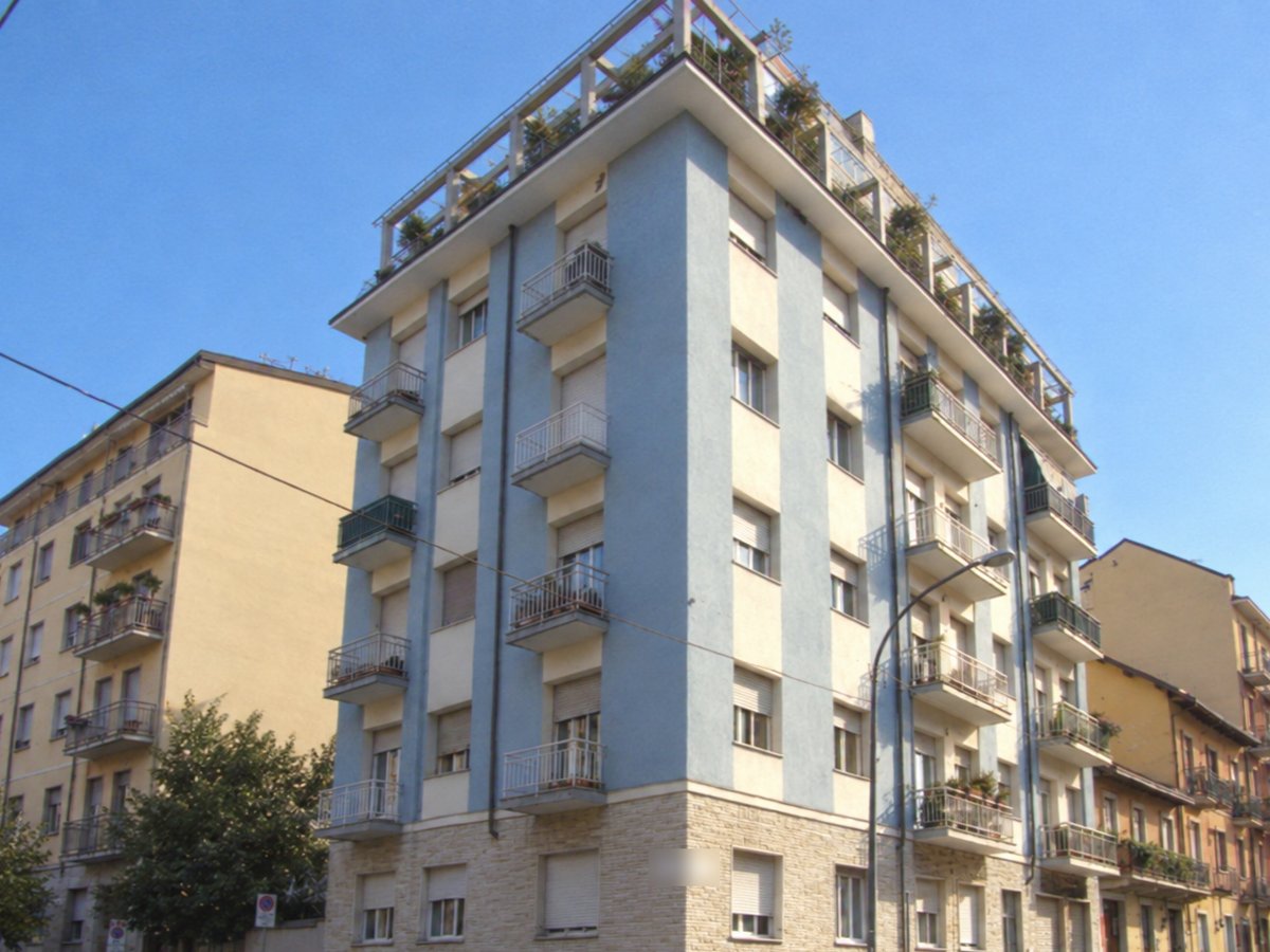 Condominio d'angolo con facciata azzurra e crema, balconi e terrazza con piante in cima