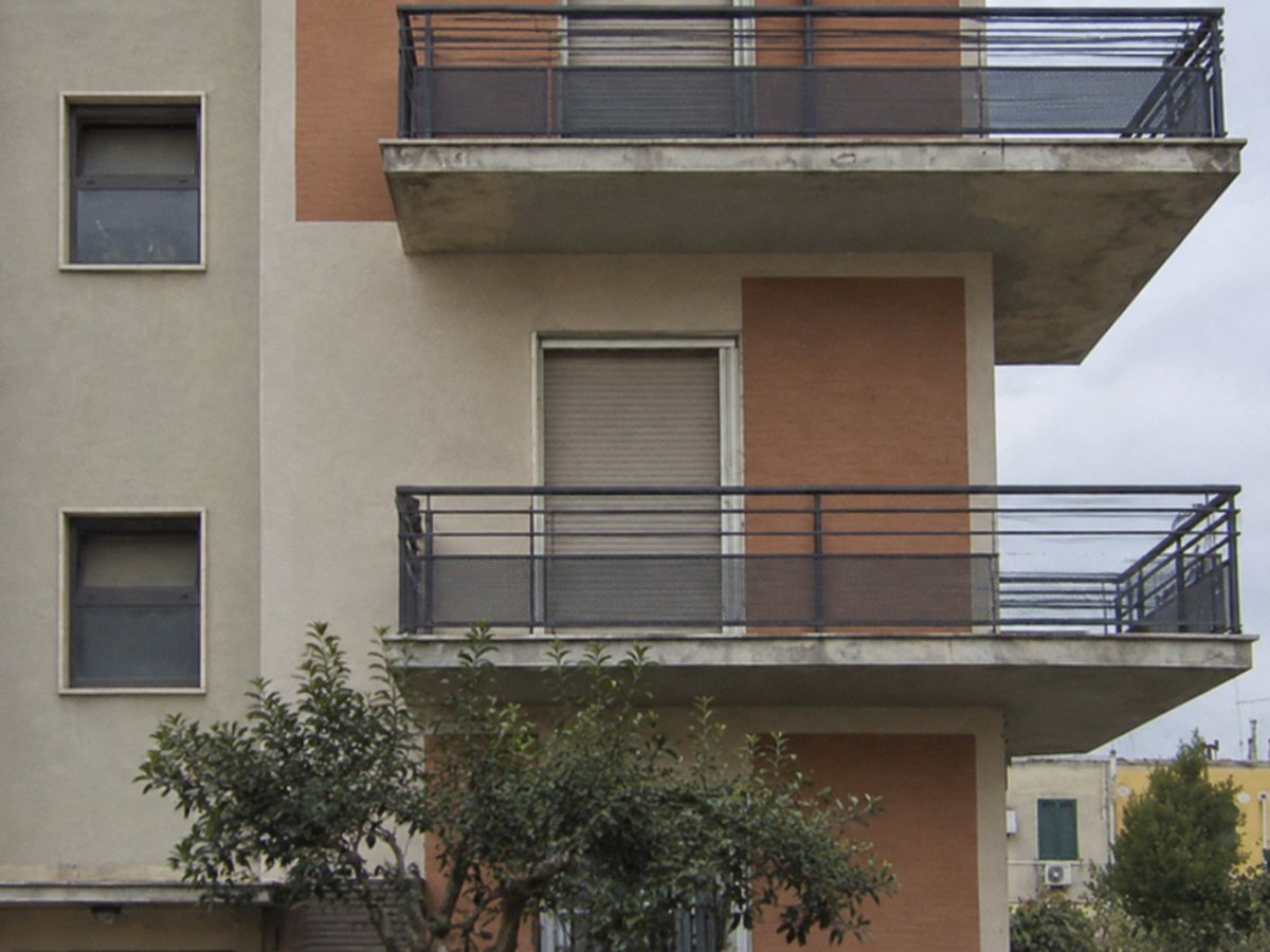 Palazzina con facciata beige e mattoni a vista, ampi balconi con ringhiera scura e un albero davanti