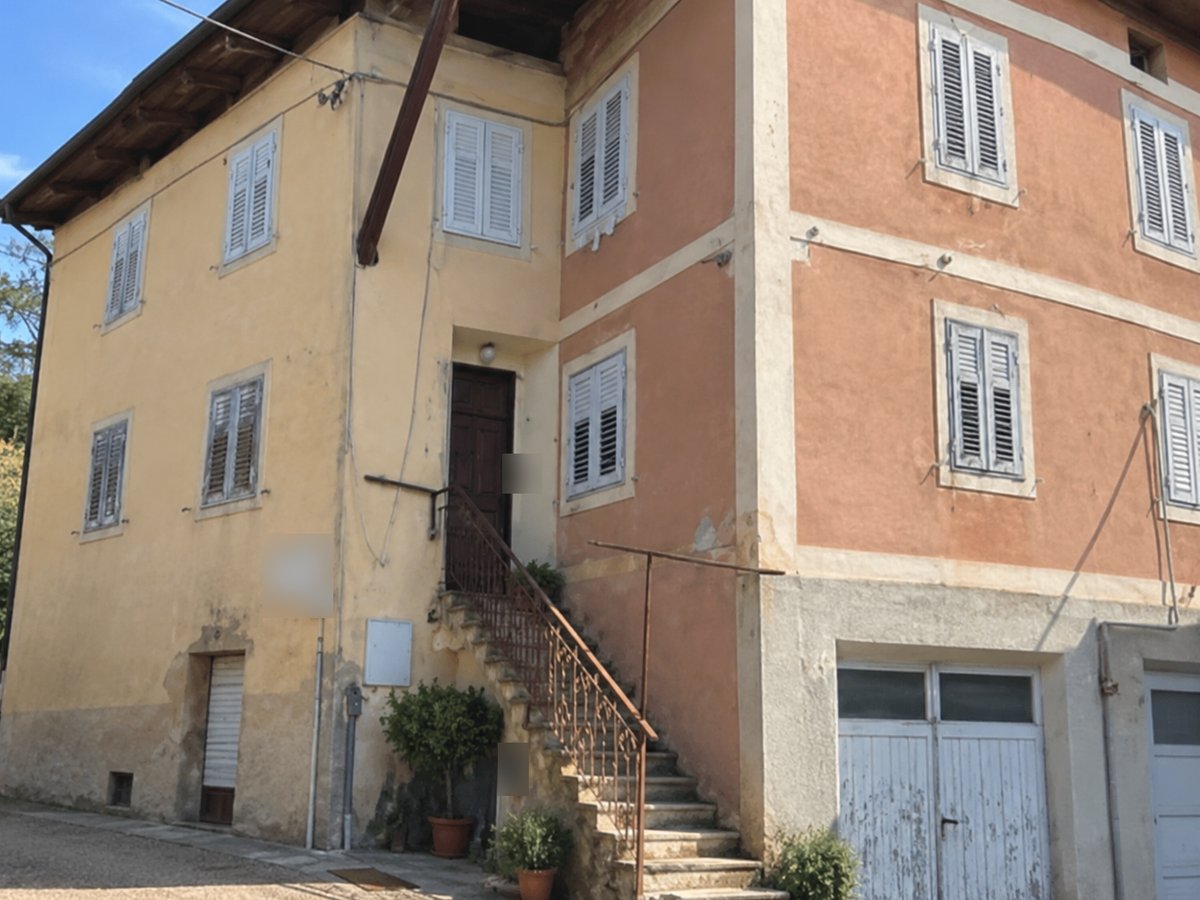 Casa su tre livelli con facciata gialla e rosa, scala esterna in pietra e garage con portone bianco