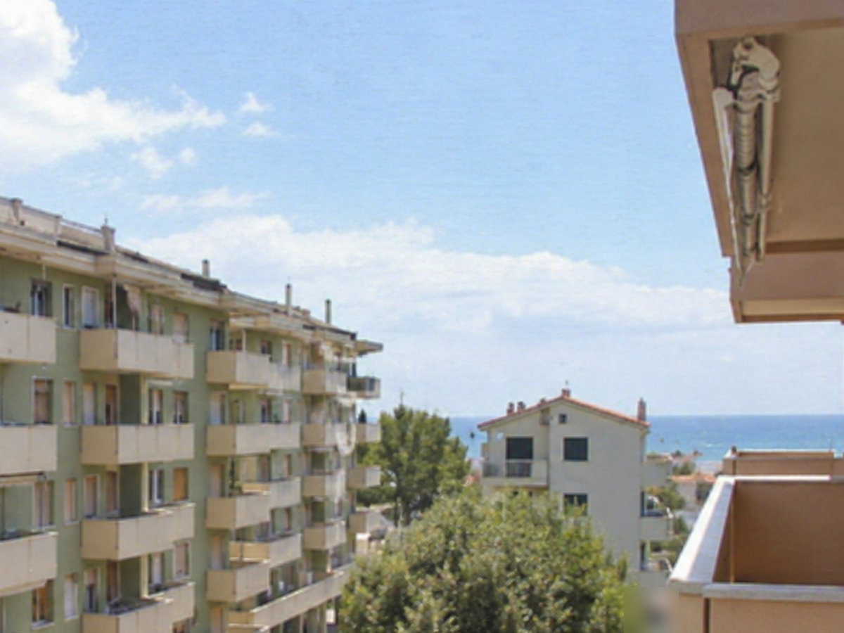 Vista dal balcone su palazzine con balconi, alberi e mare all’orizzonte