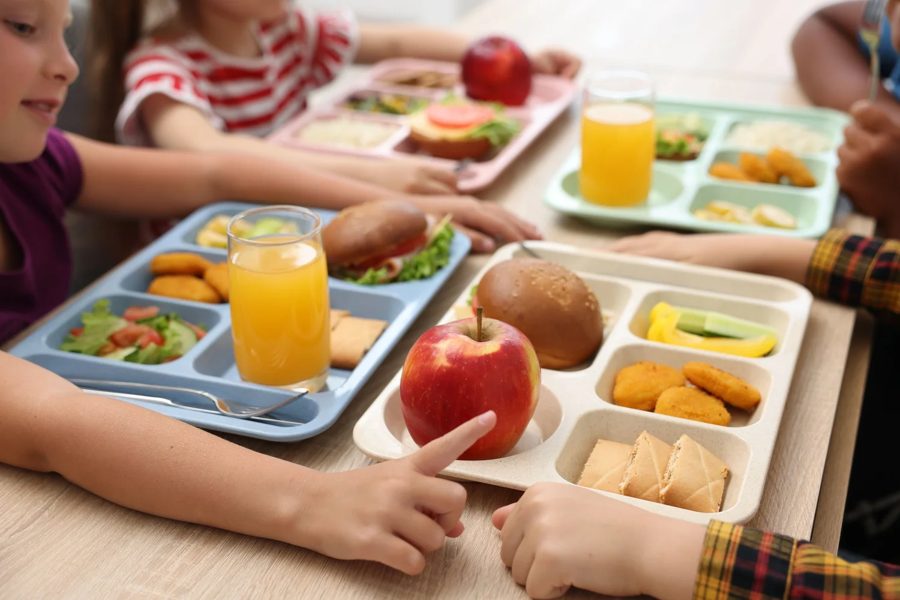 Estudiantes comparten bandejas de almuerzo con fruta y sándwiches