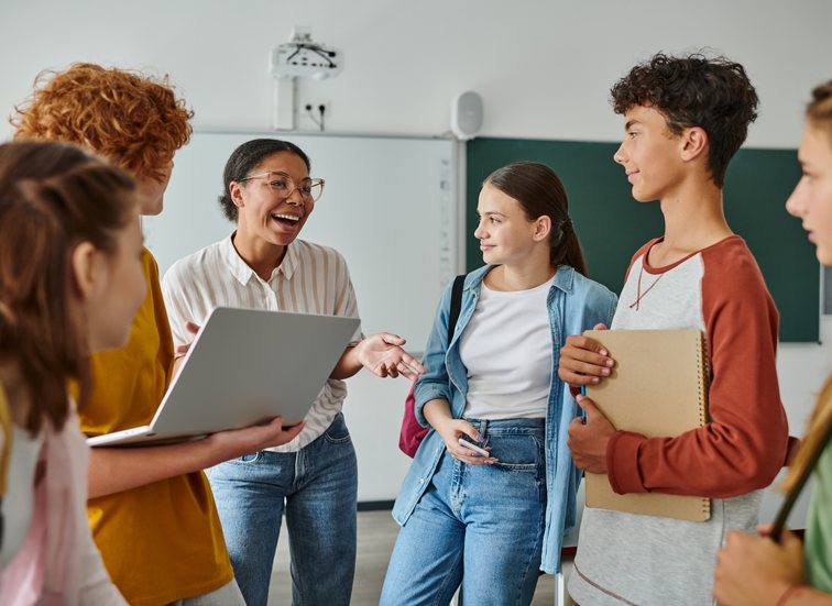 A teacher and students smiling and talking as the school day begins