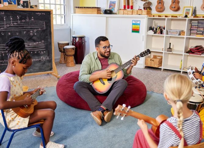 A teacher plays guitar with students holding ukuleles and drums