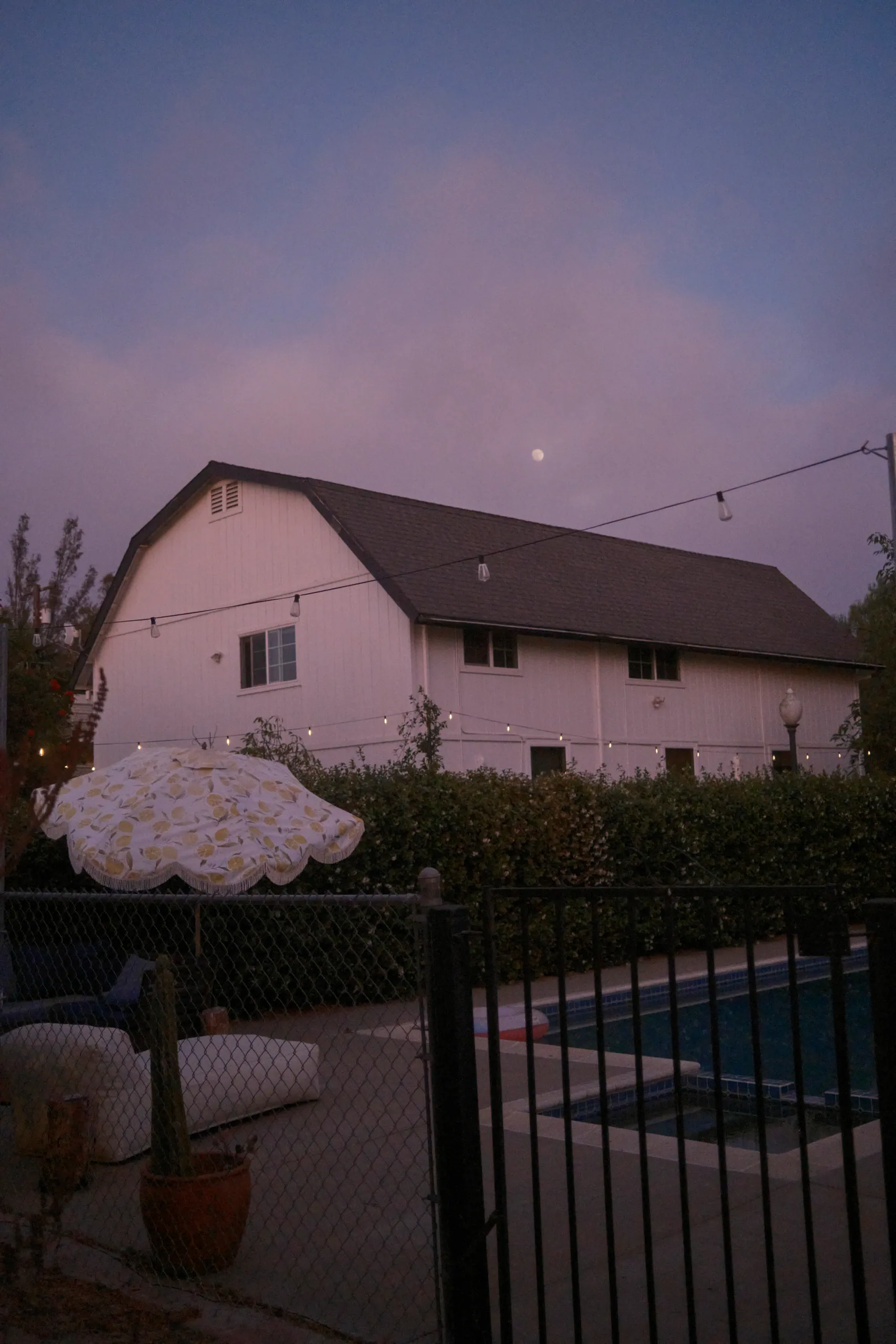 White barn with a dark roof above the saltwater pool at dusk, with the moon in a lavender sky
