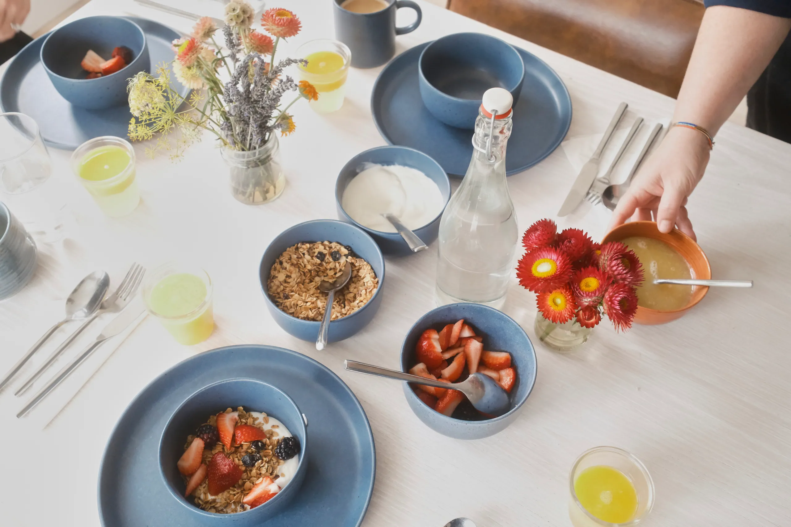 Overhead view of a breakfast table with bowls of fruit, granola, yogurt, coffee and strawflowers