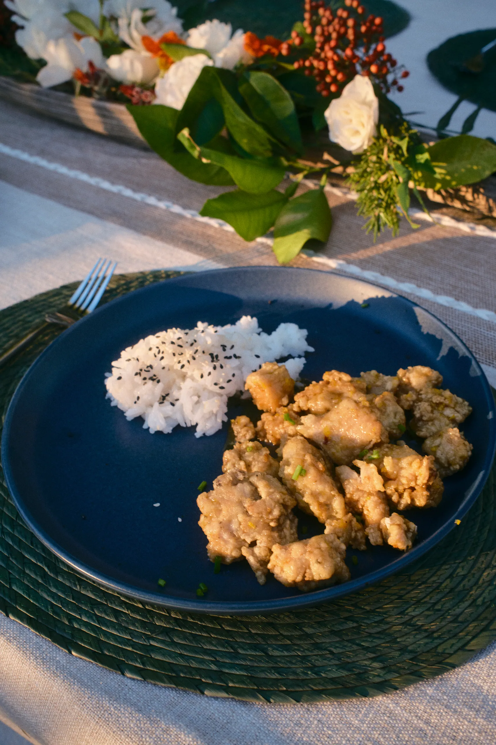 Dinner plate of crispy fried bites and white rice with black sesame beside a white flower centerpiece