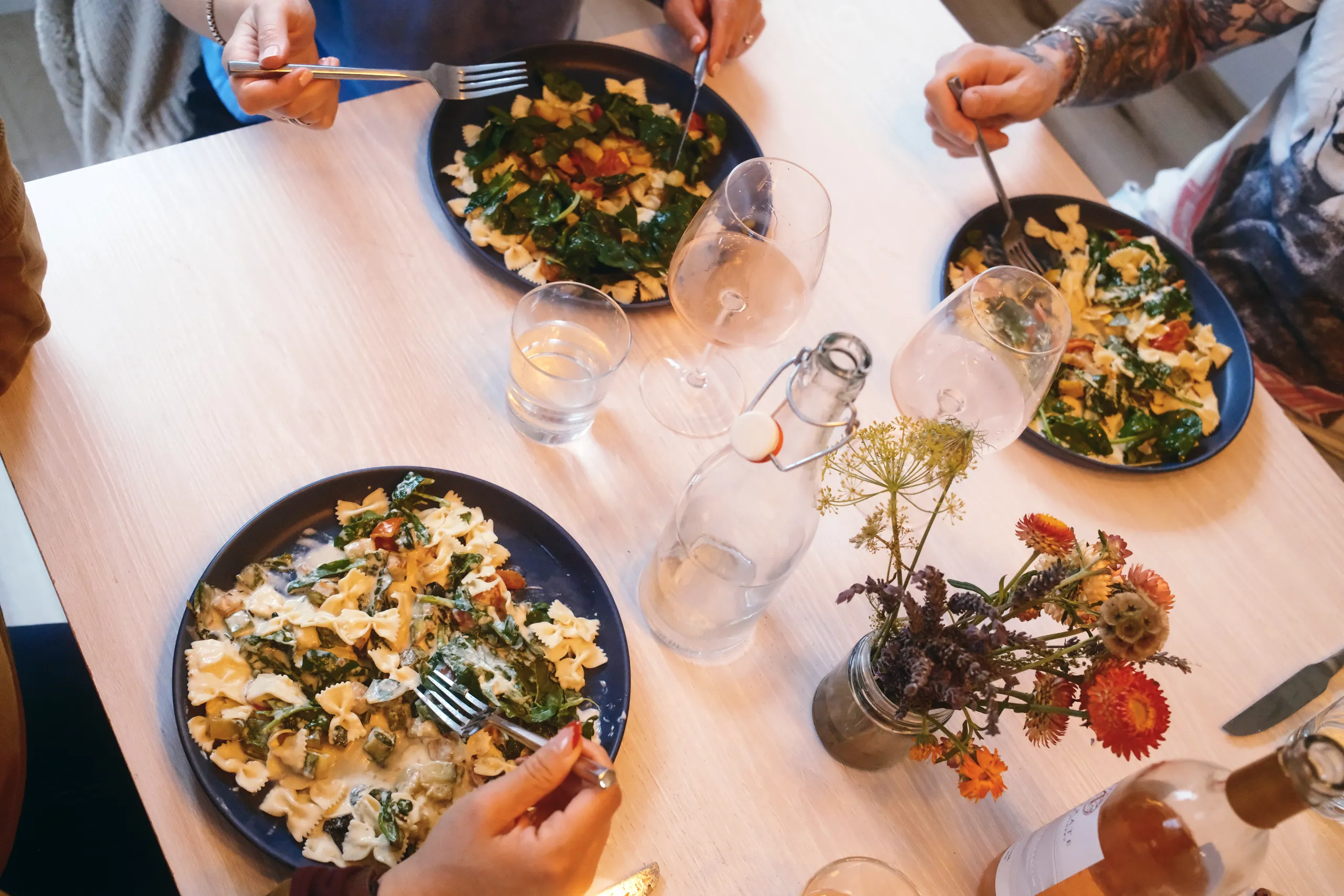 Overhead view of guests eating bowtie pasta and salads around a white table with flowers