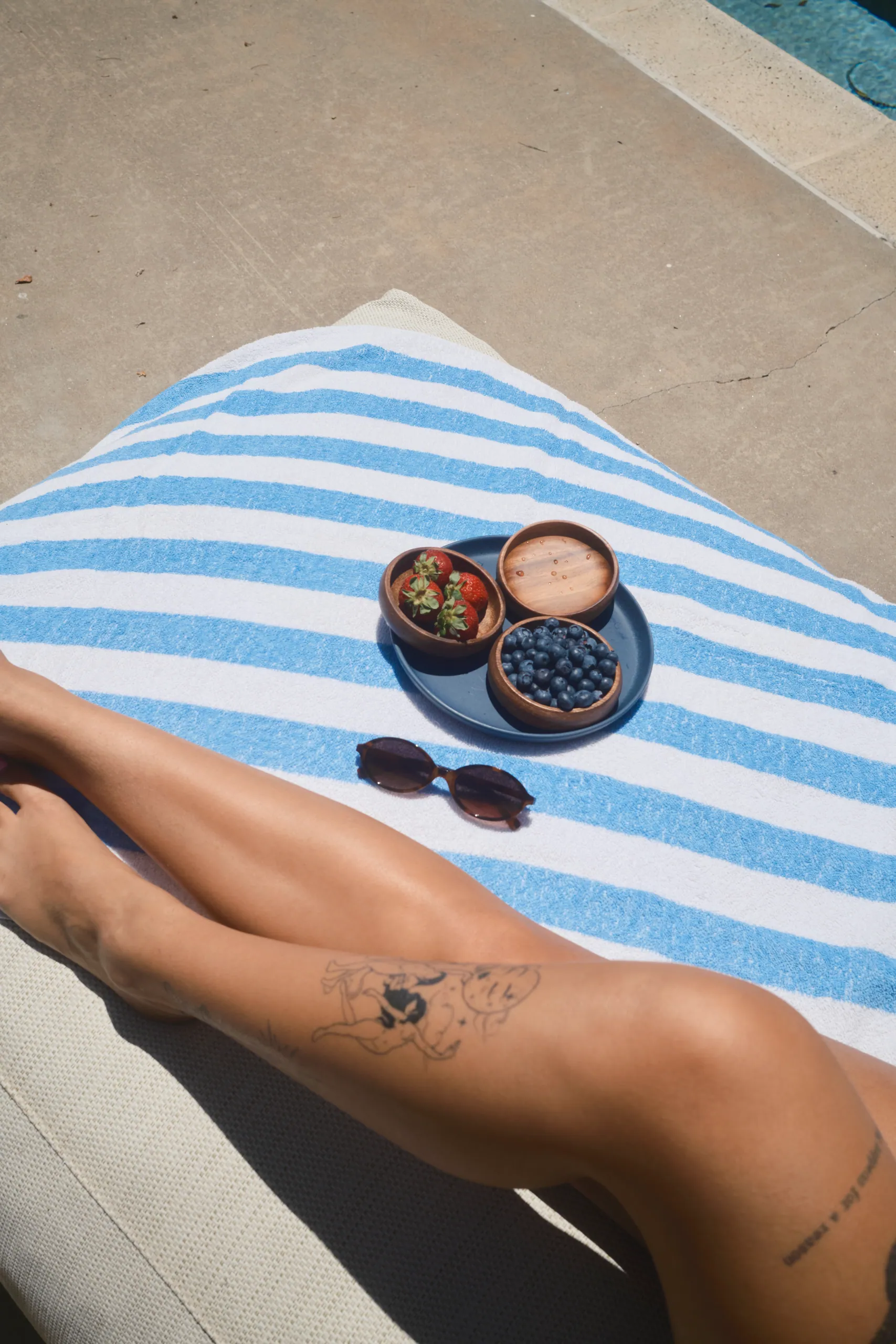 Woman's legs stretched out on a pool lounger next to bowls of berries and sunglasses