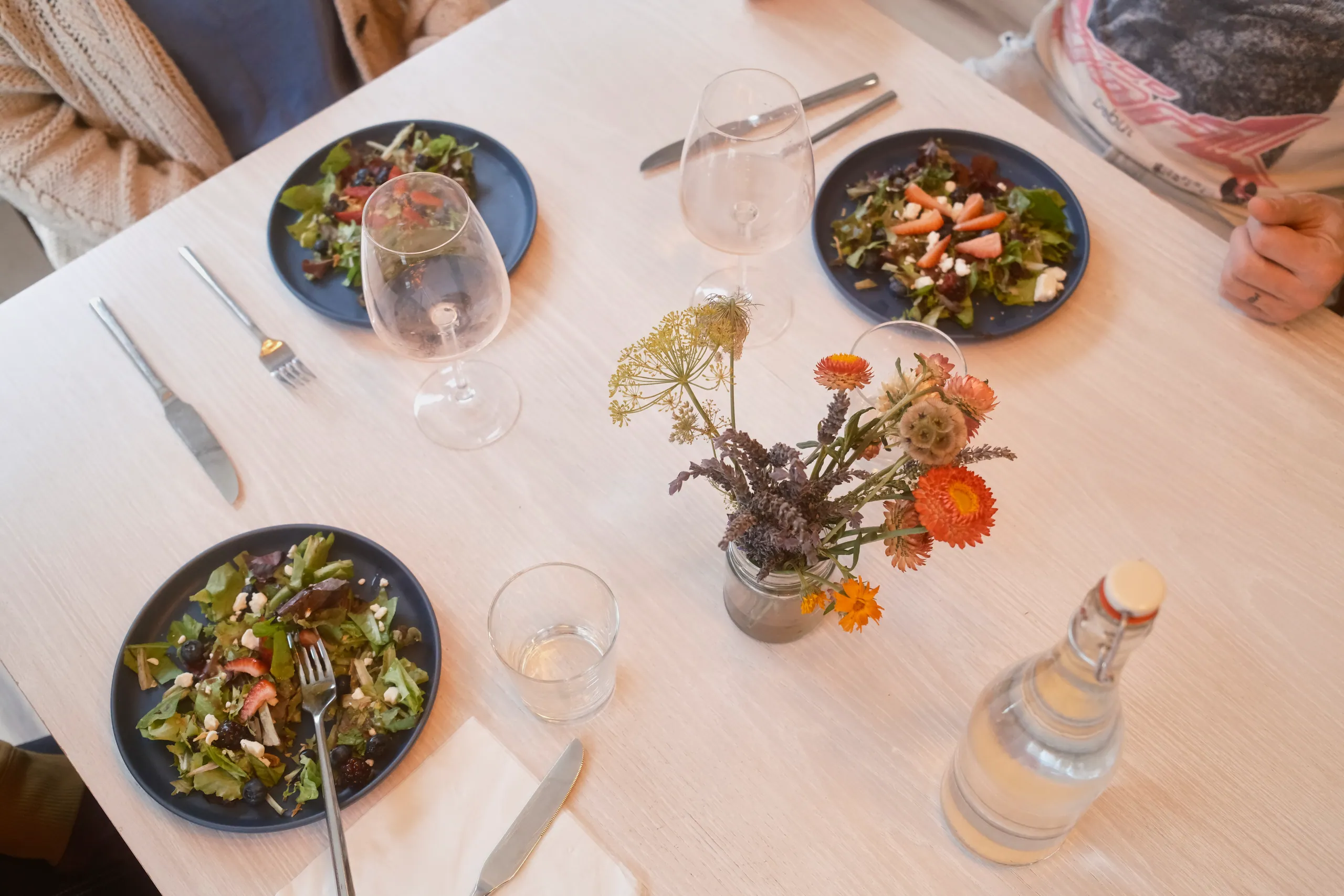 Overhead view of salads, glasses and a small wildflower bouquet on a white dining table