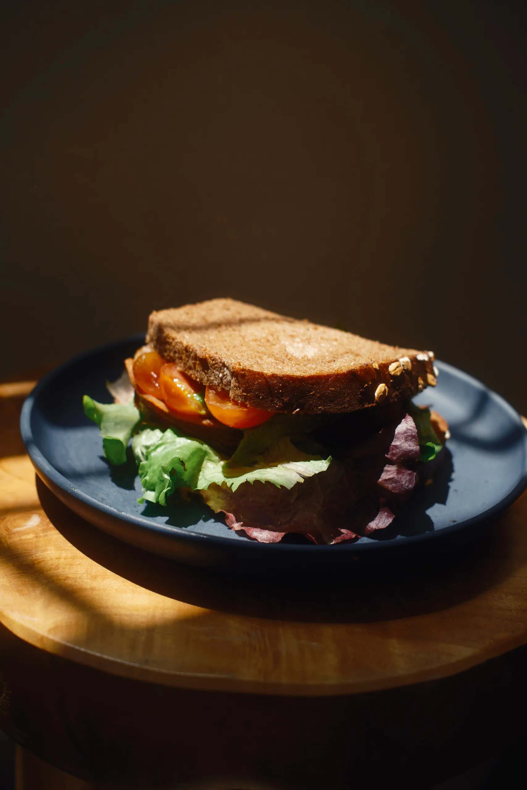 Whole-grain sandwich with tomato and fresh greens on a blue plate on a wooden side table
