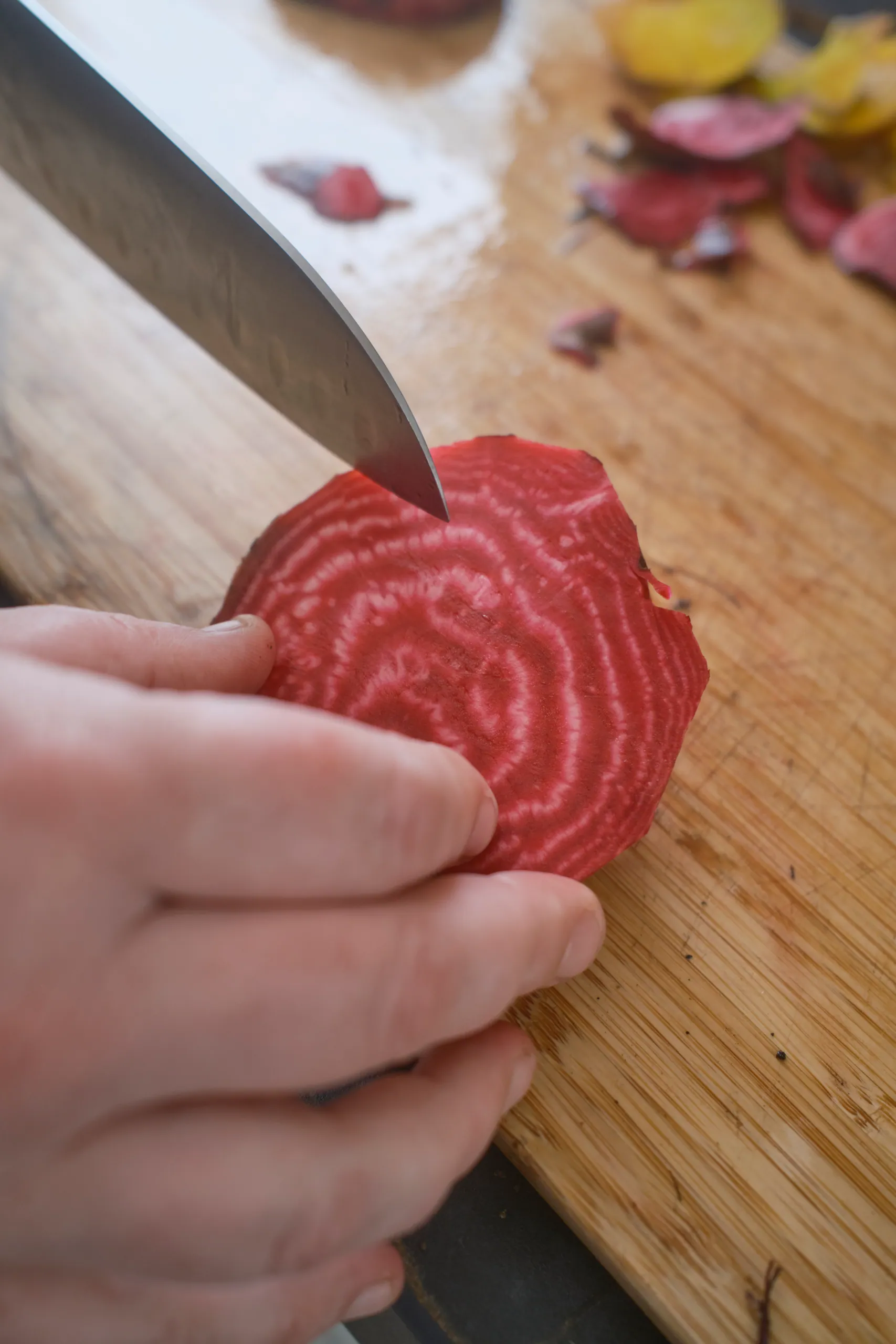 Hand slicing a candy-striped Chioggia beet on a wooden cutting board