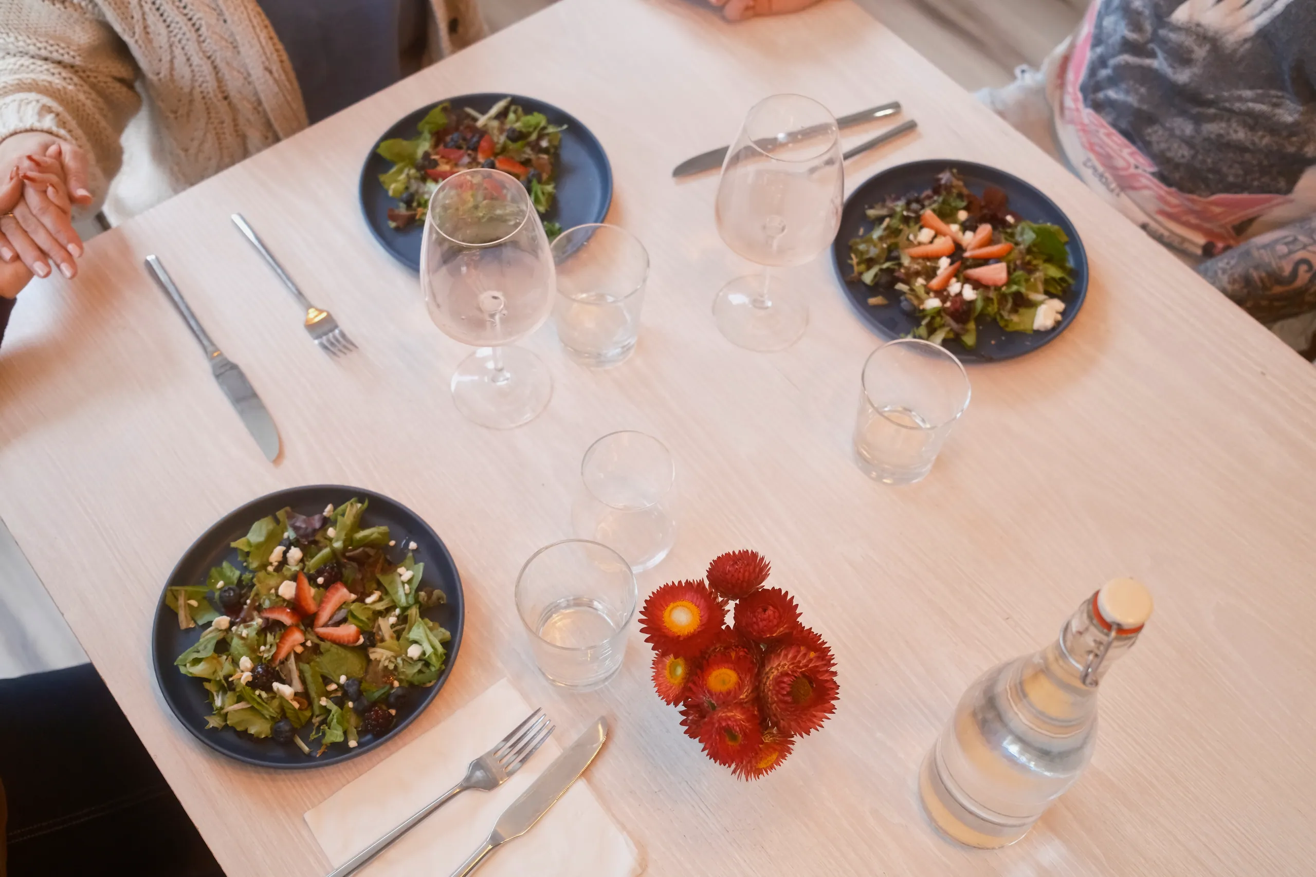 Overhead view of a dining table set with berry salads, wine glasses and red strawflowers
