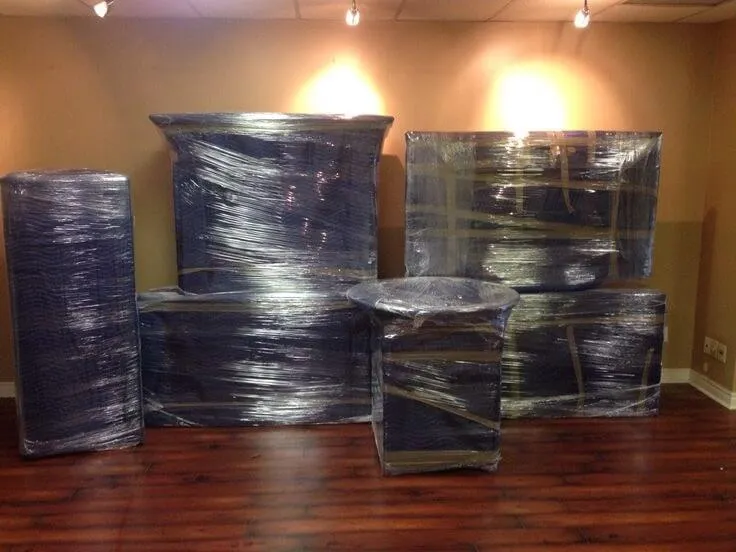 Large furniture pieces shrink-wrapped and staged for a move on a wood floor