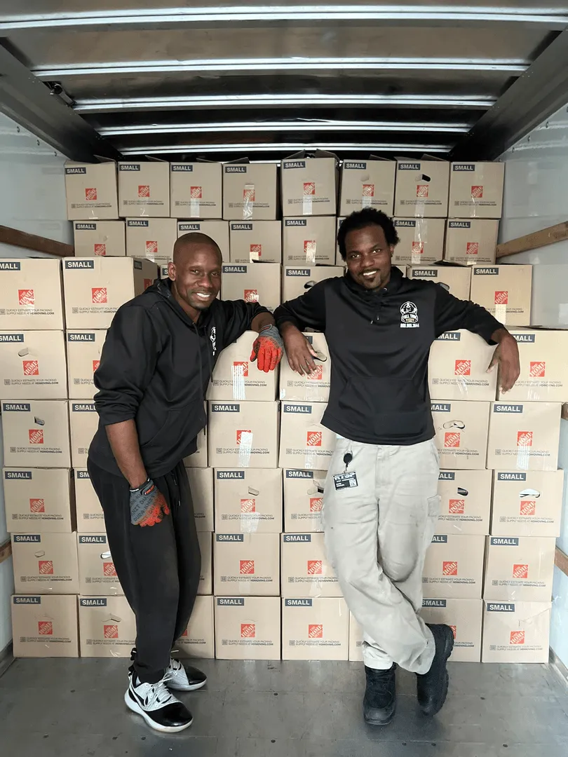 Two Full Time Movers Labor Professionals standing in a truck packed with stacked moving boxes