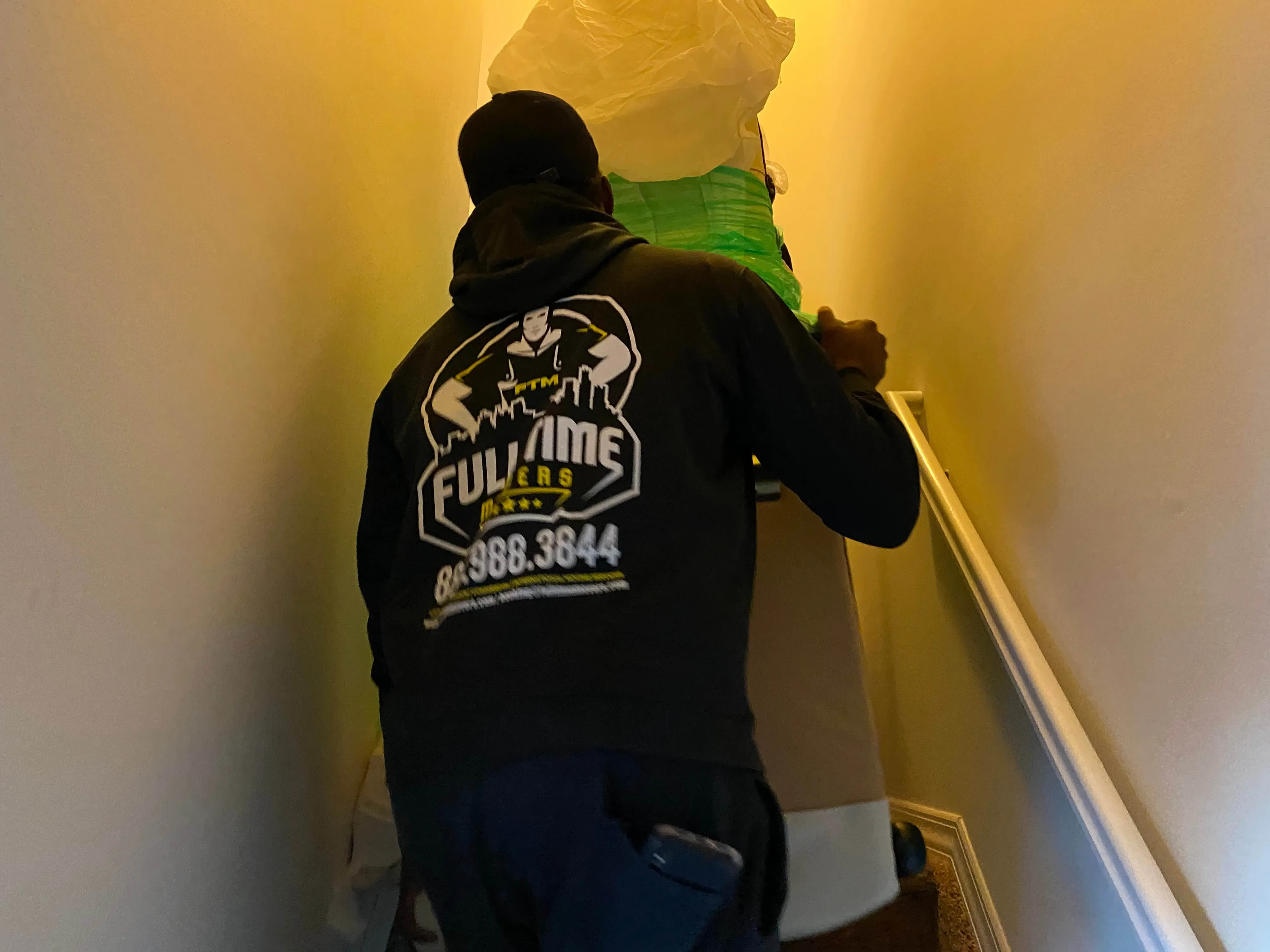 Full Time Movers crew member carrying a wrapped item up a narrow staircase