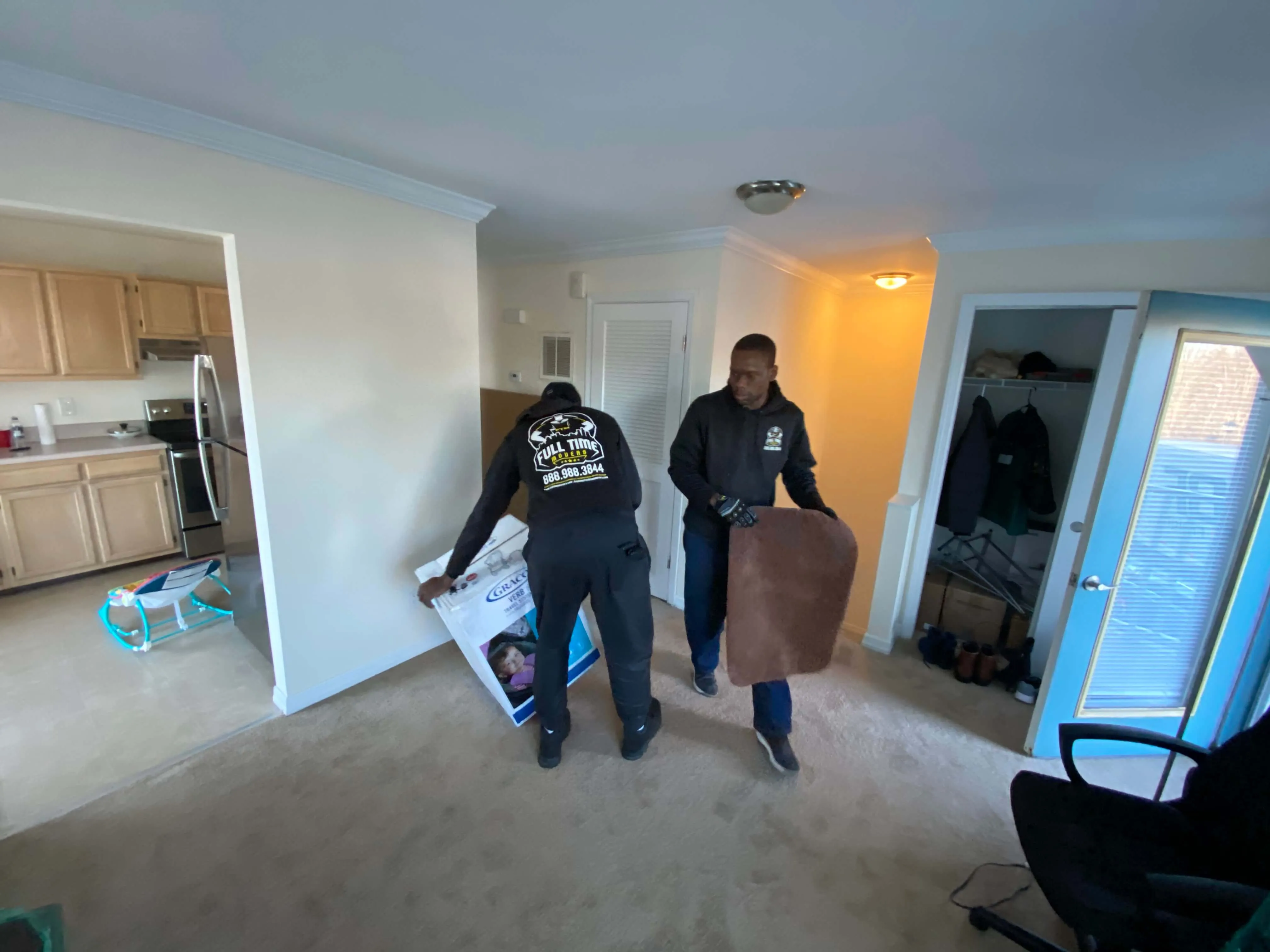 Two Full Time Movers crew members carrying items through an apartment living room