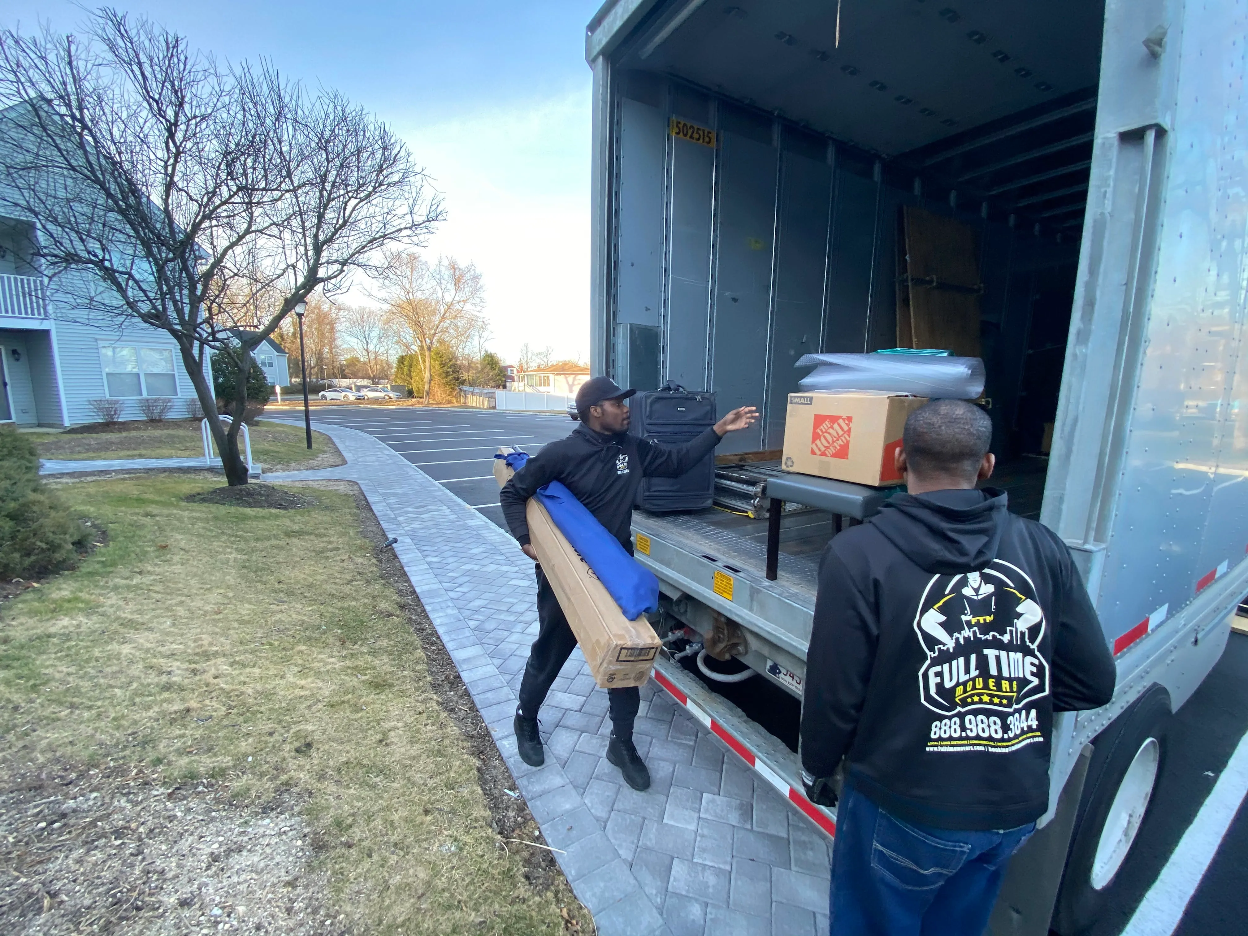 Full Time Movers Labor Professionals loading a rolled rug and boxes into the back of a moving truck
