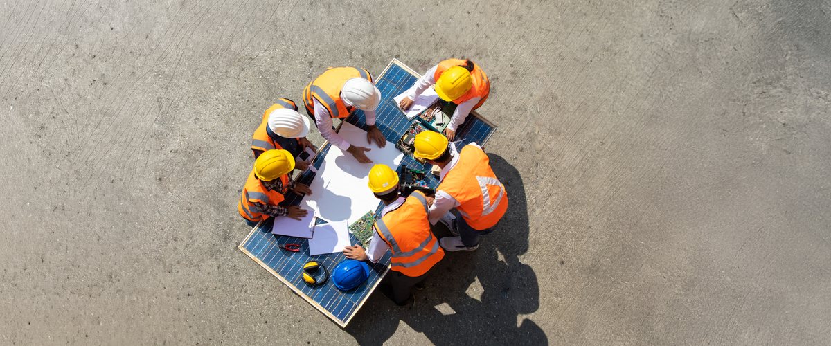 Field crew in hard hats reviewing plans from above