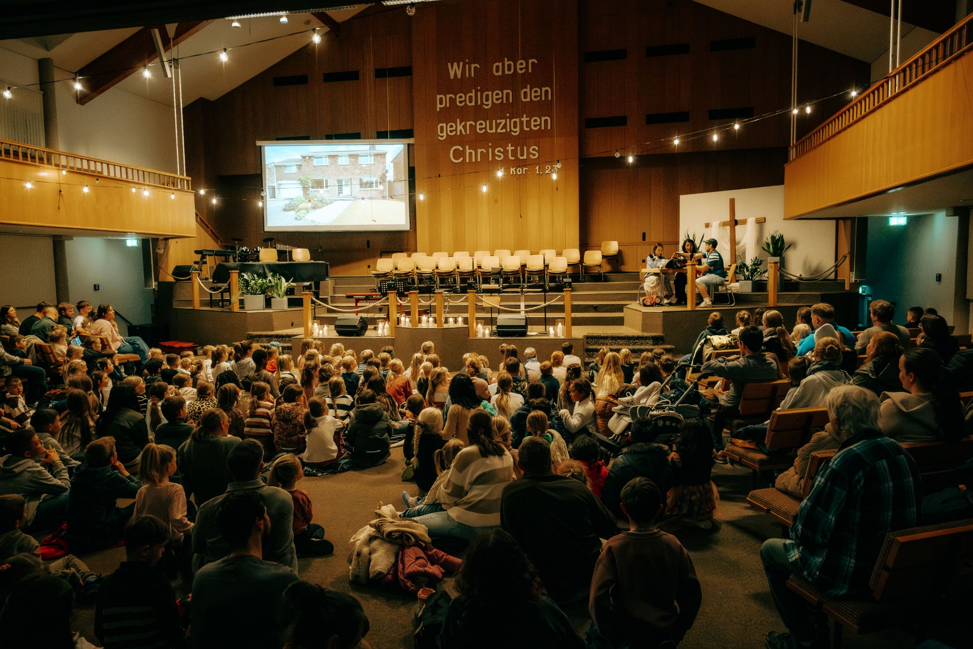 Viele Kinder und Familien sitzen beim Lichterfest im Gemeindesaal der EBBP Pfungstadt und schauen gespannt zur Bühne unter Lichterketten