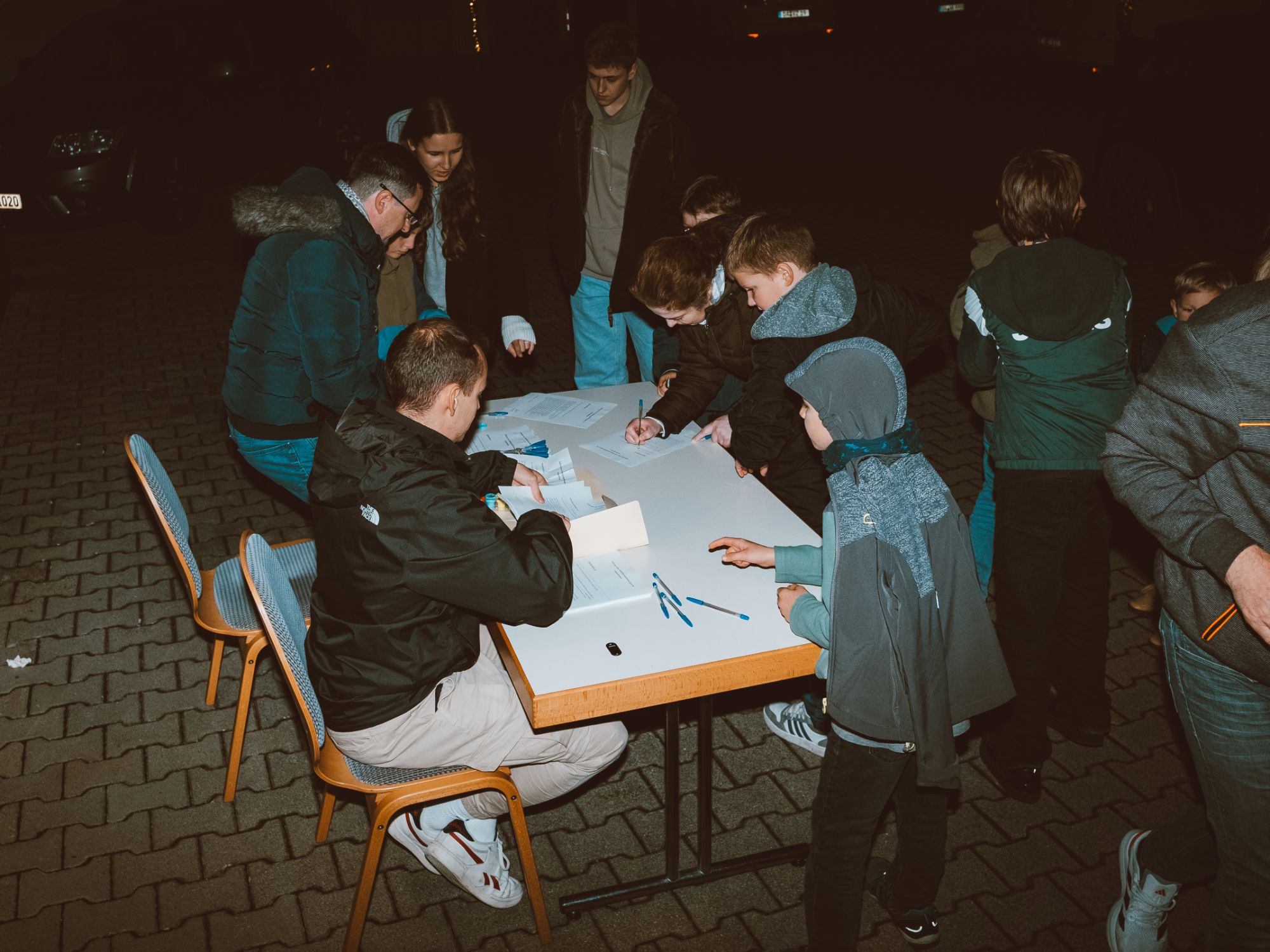 Kinder und Jugendliche füllen beim Lichterfest an einem Tisch gemeinsam Spielzettel aus