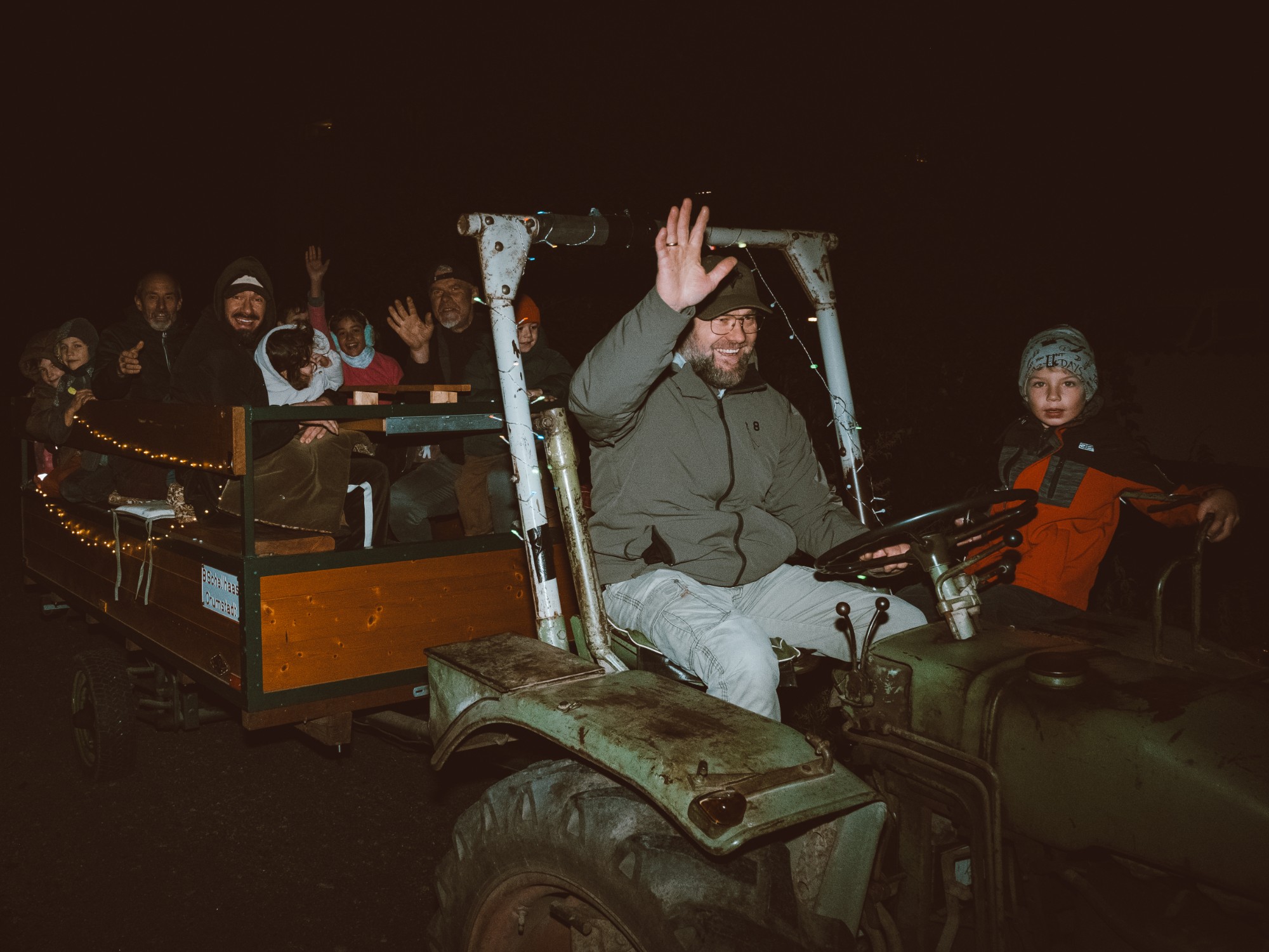 Ein Fahrer winkt vom Traktor, auf dem beleuchteten Anhänger fahren fröhliche Kinder und Erwachsene beim Lichterfest mit
