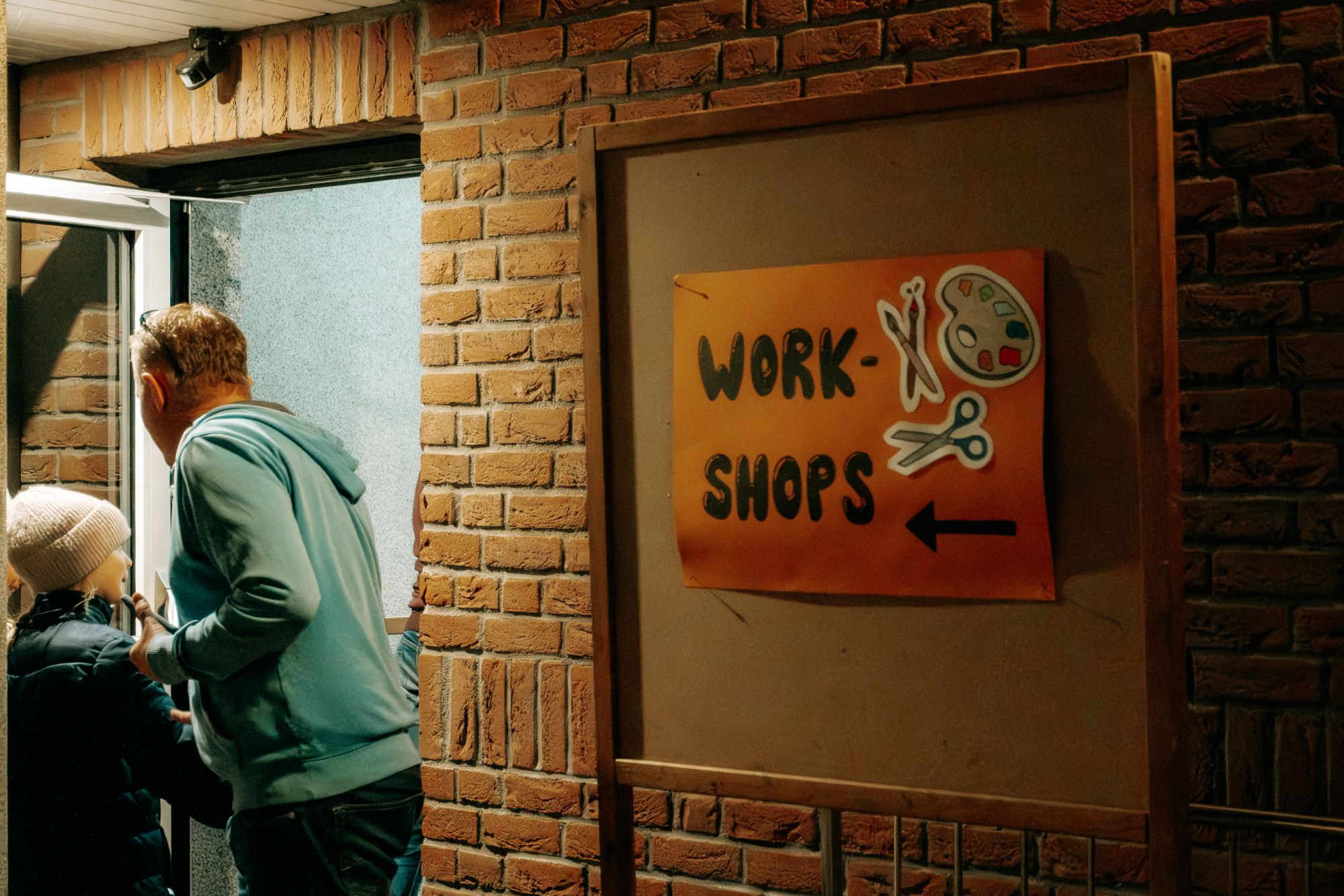 Ein orangefarbenes Schild weist an der Backsteinwand den Weg zu den Workshops