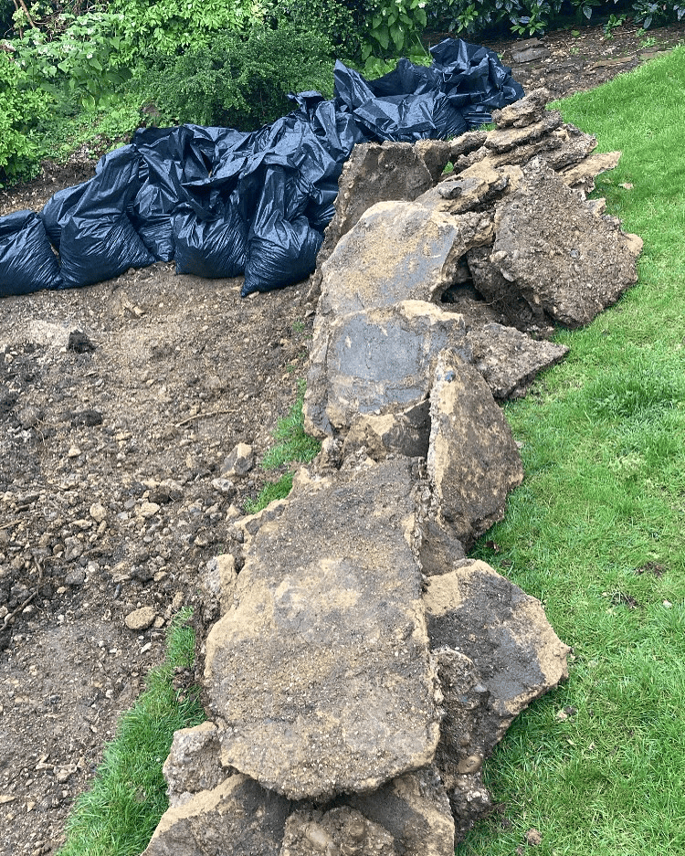 Broken concrete slabs on a lawn with black bags of soil behind