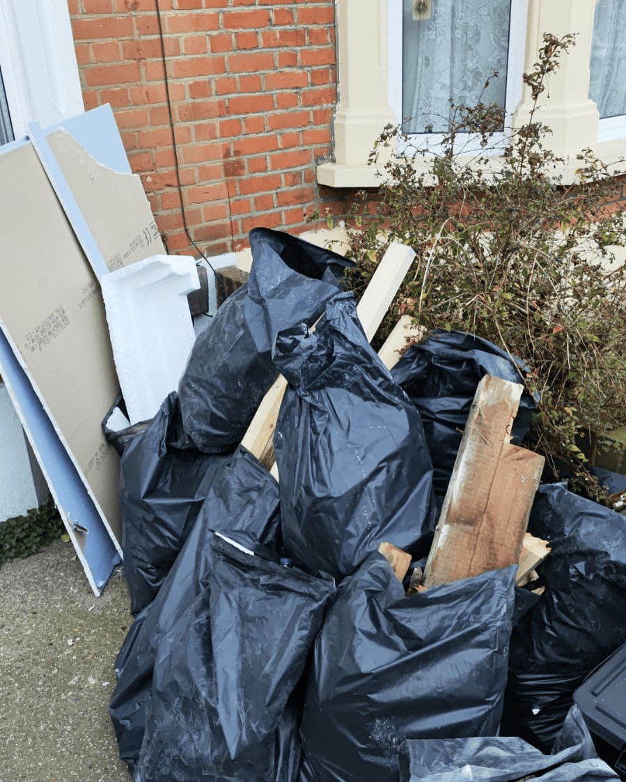 Black bags, timber and plasterboard sheets outside a brick house