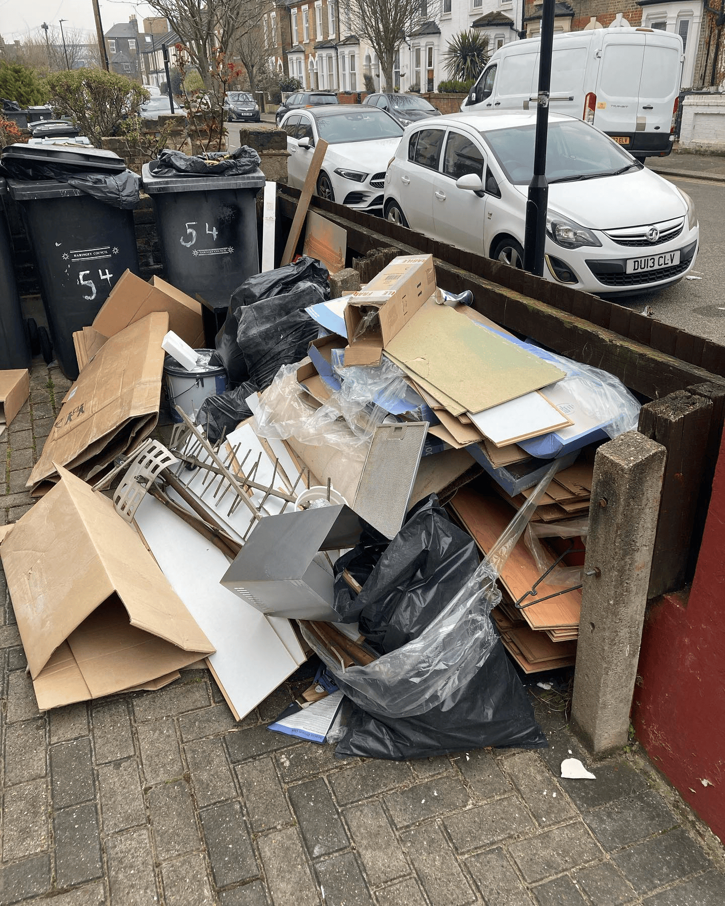 Boards, packaging, plastic and bags piled by the front wall of a terraced house