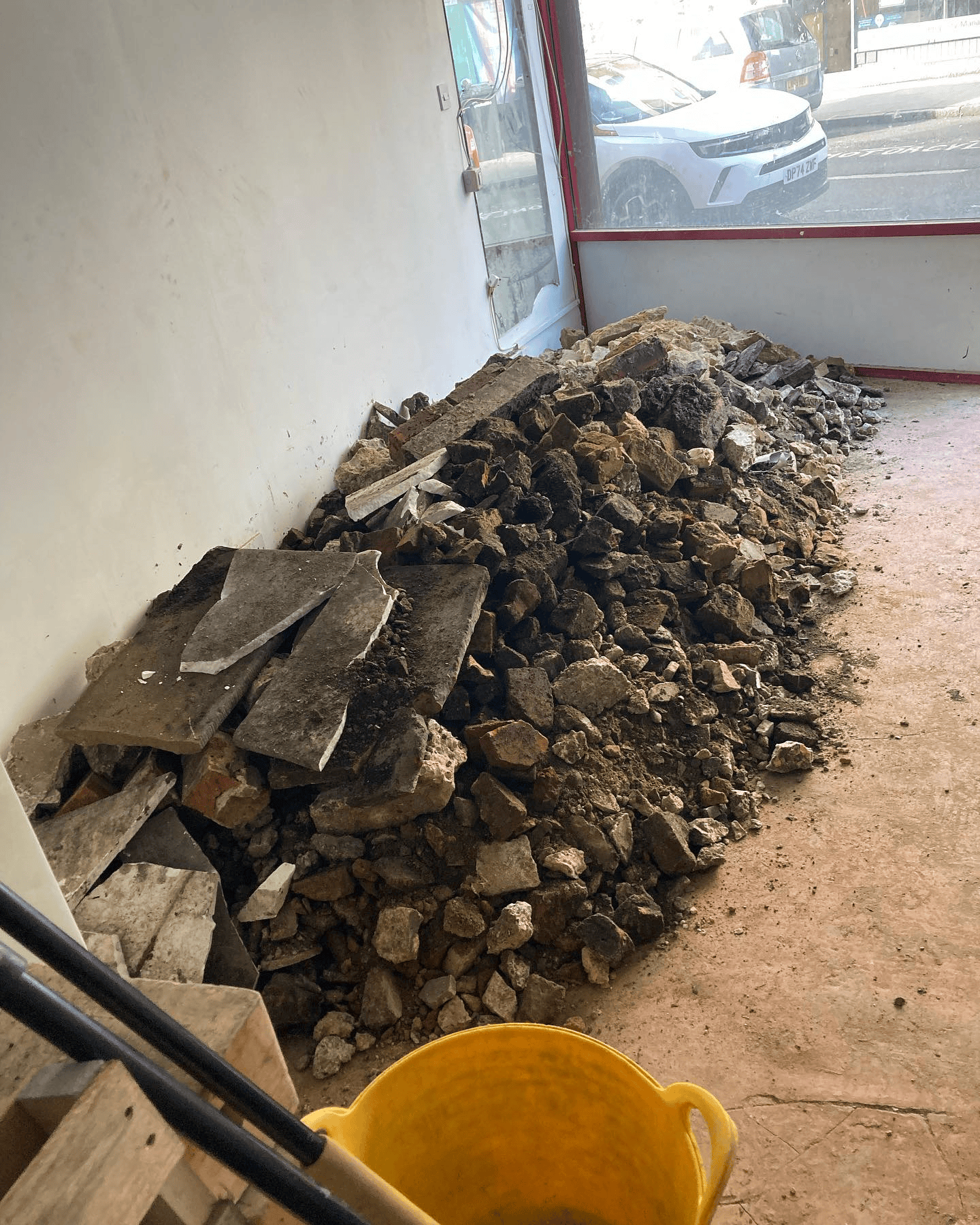 Rubble and broken paving slabs inside an empty shop unit next to a yellow bucket