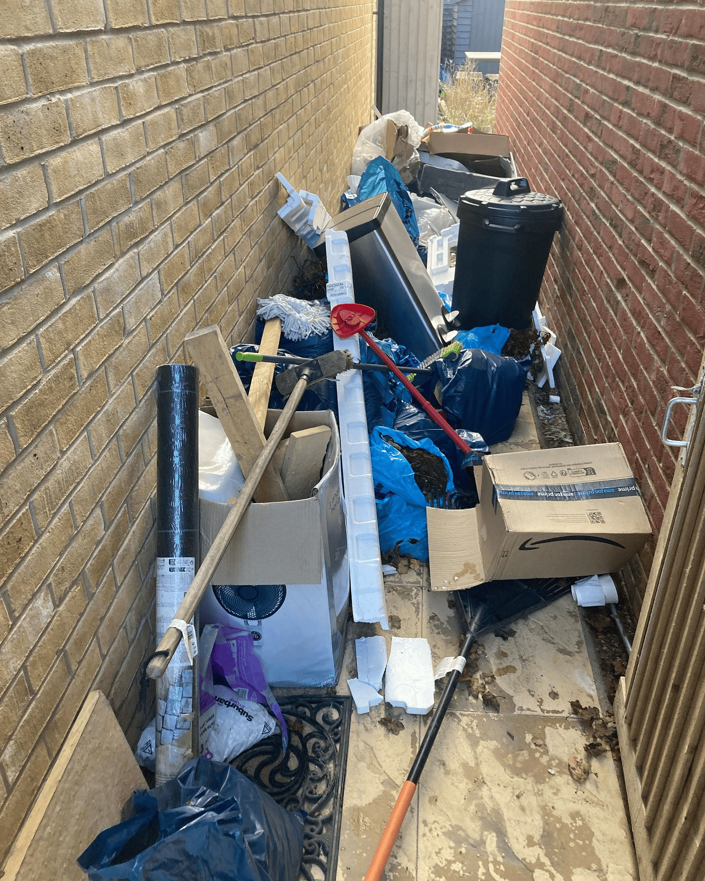 Side passage of a house filled with bags, boxes and household rubbish before a clearance