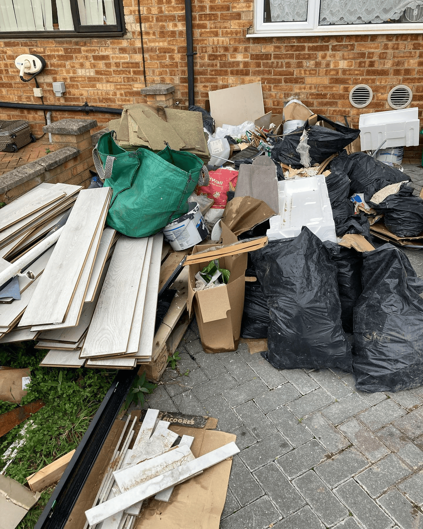 Laminate flooring, boxes and black bags piled on a block paved driveway, ready for clearance