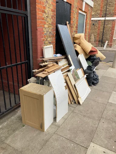 Kitchen units, boards, a mattress and black bags stacked against a building on a pavement