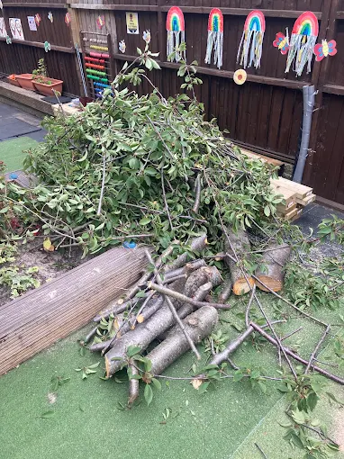 Cut tree branches and logs piled on artificial grass in a back garden