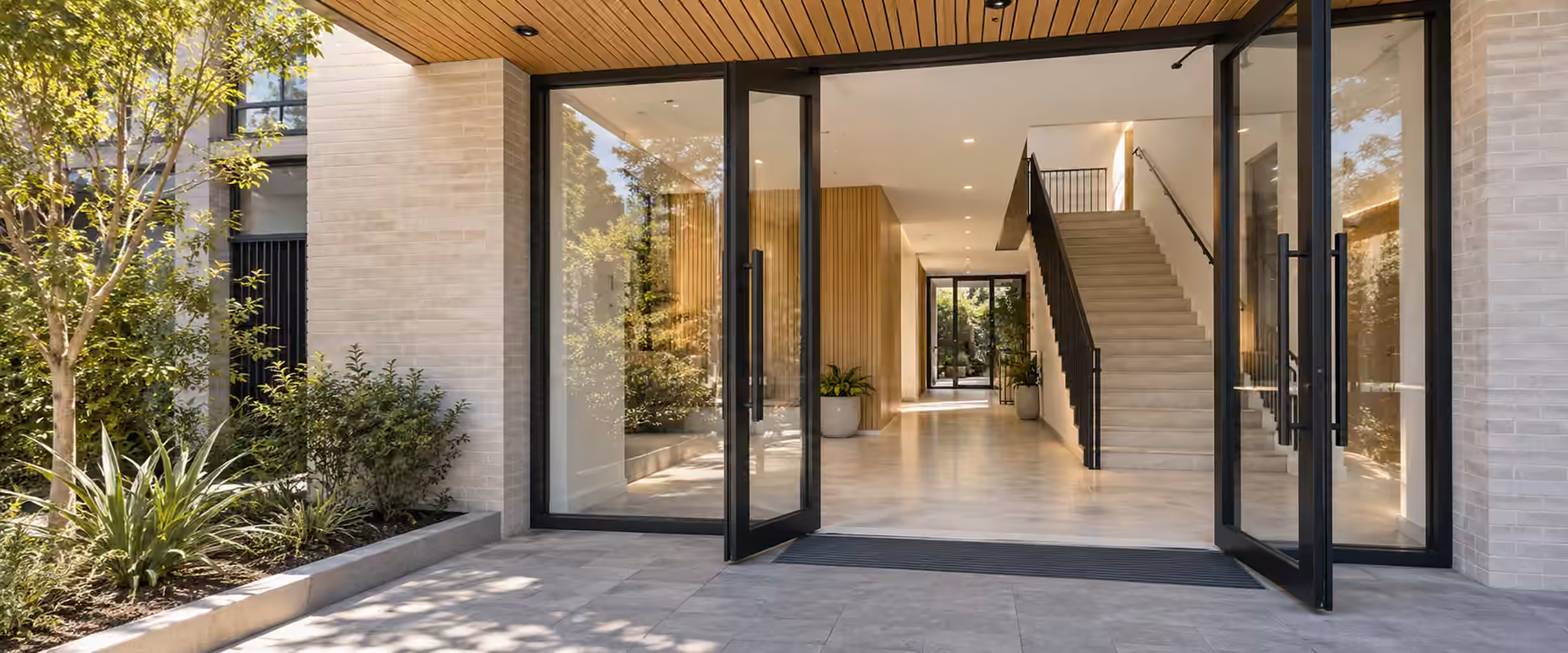 Open glass doors into a completed home with a timber-lined ceiling and a floating staircase
