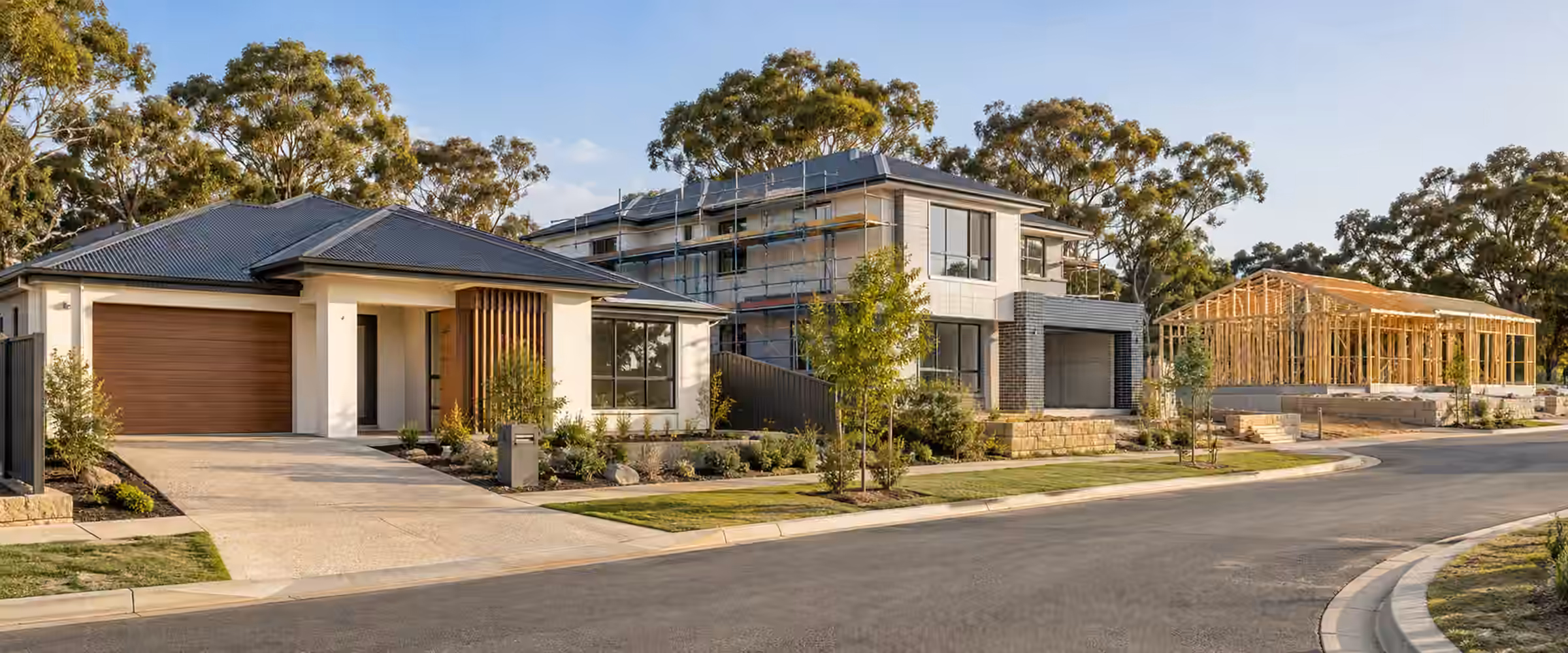 Residential street with a finished home, a two-storey home under scaffolding and a timber frame going up