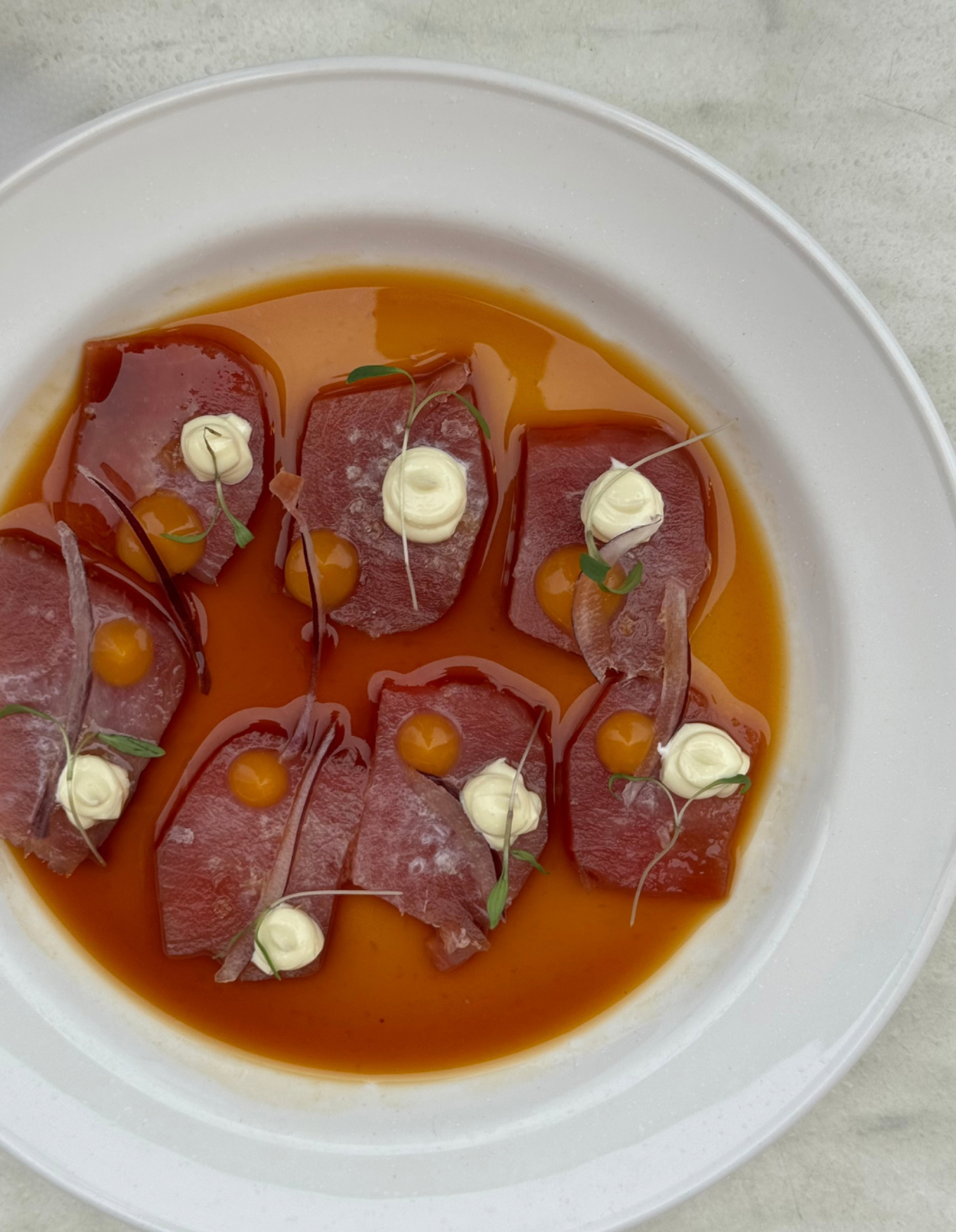 Sliced raw fish in a bright broth on a white plate