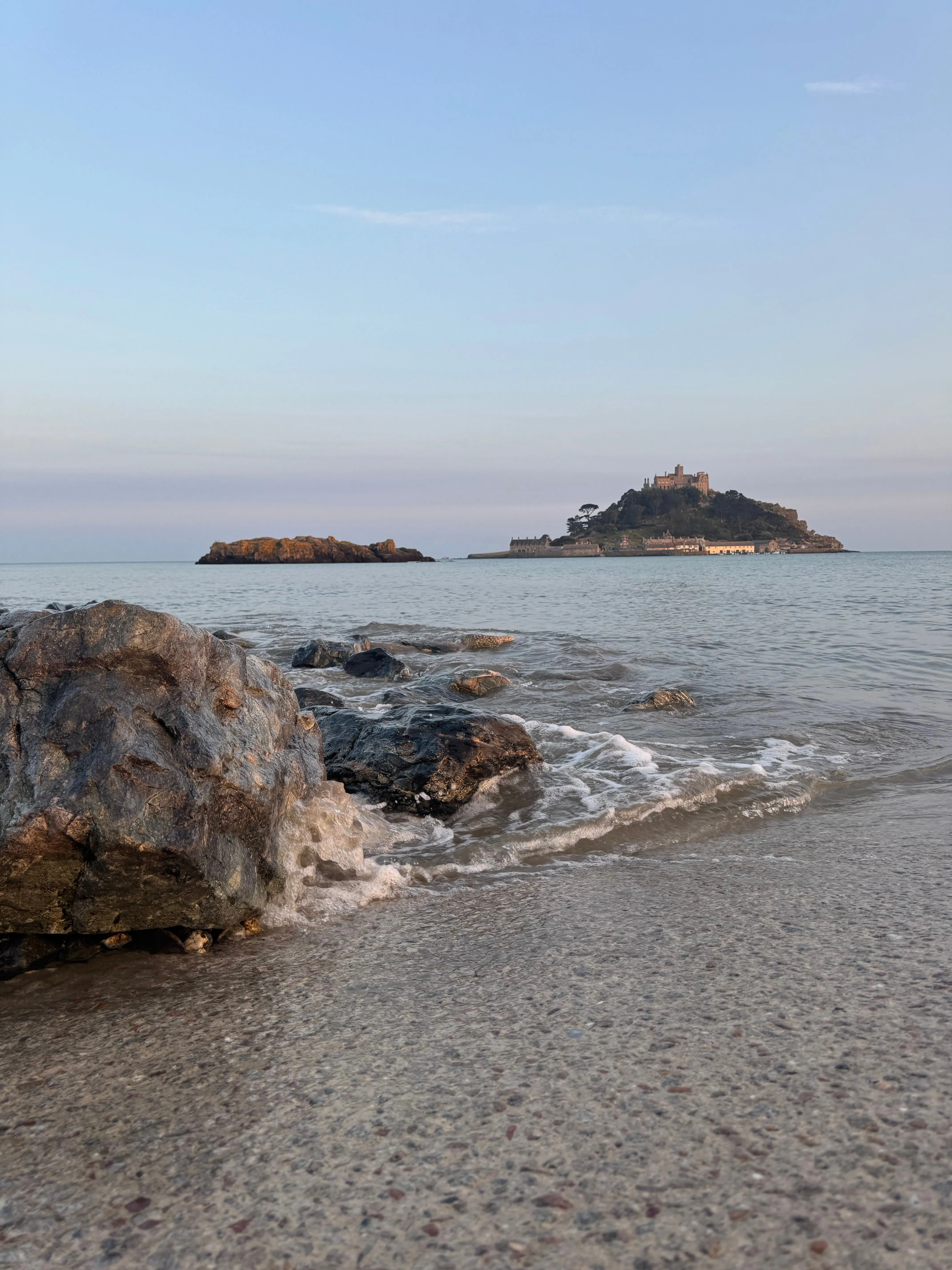 St Michael's Mount in the distance beyond rocks and shallow waves at dusk