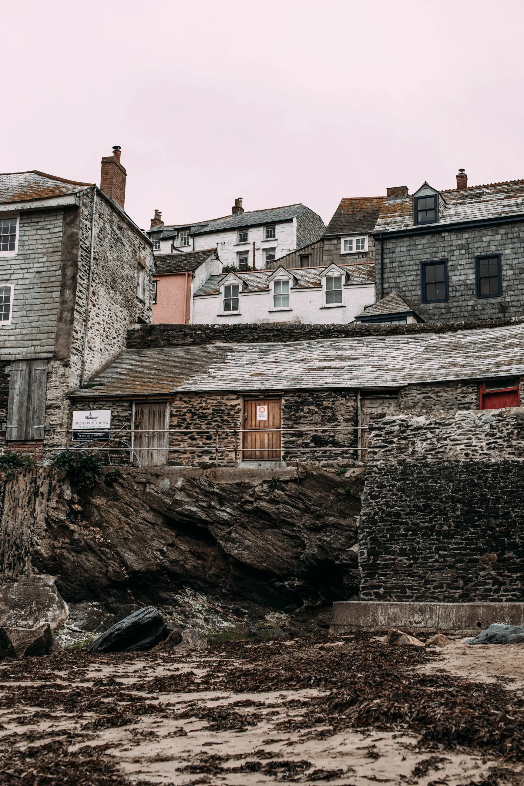 Slate and stone fishermen's cottages above rocky beach with seaweed, overcast sky
