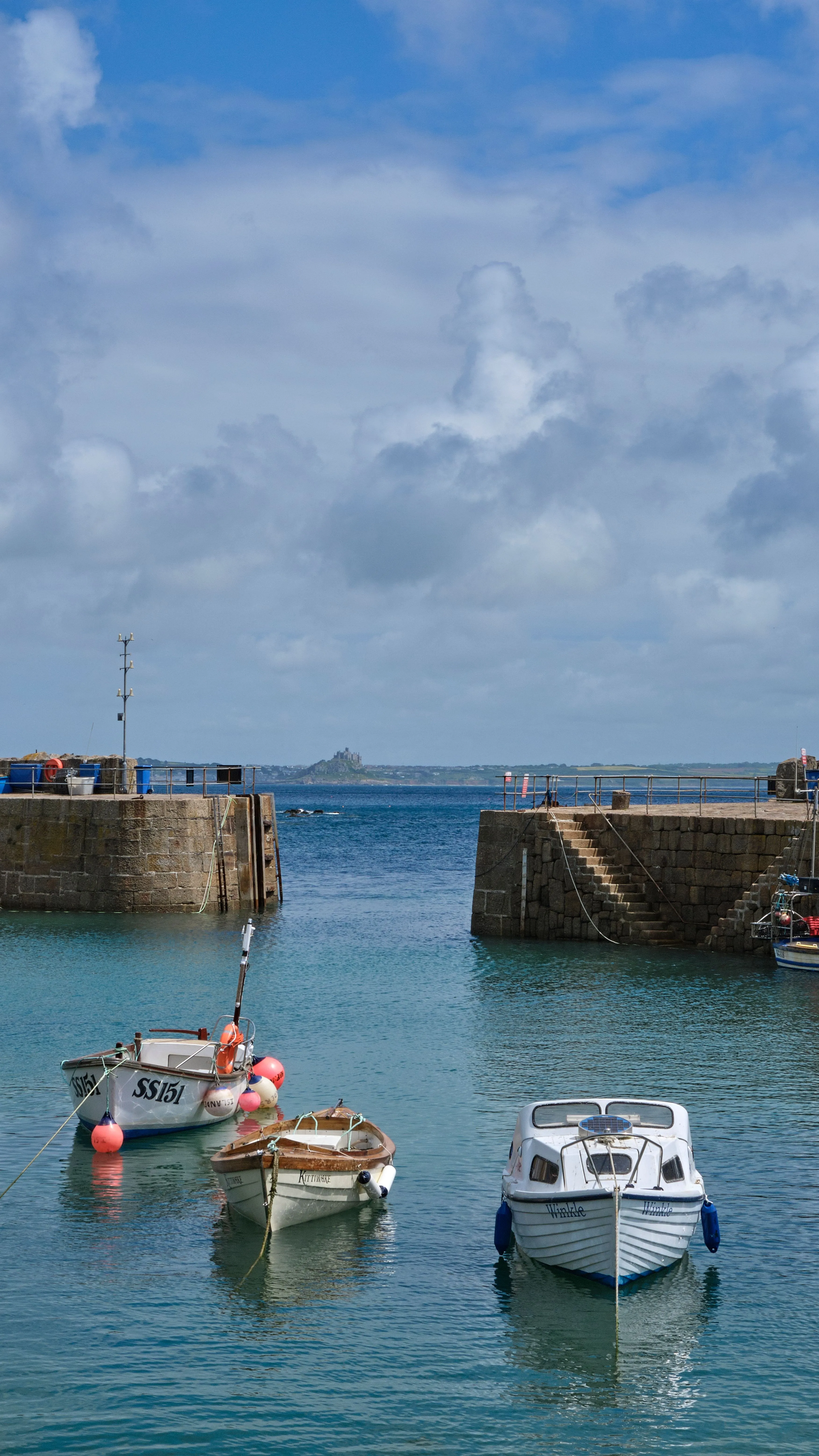 Small boats moored in a Cornish harbour entrance between stone walls