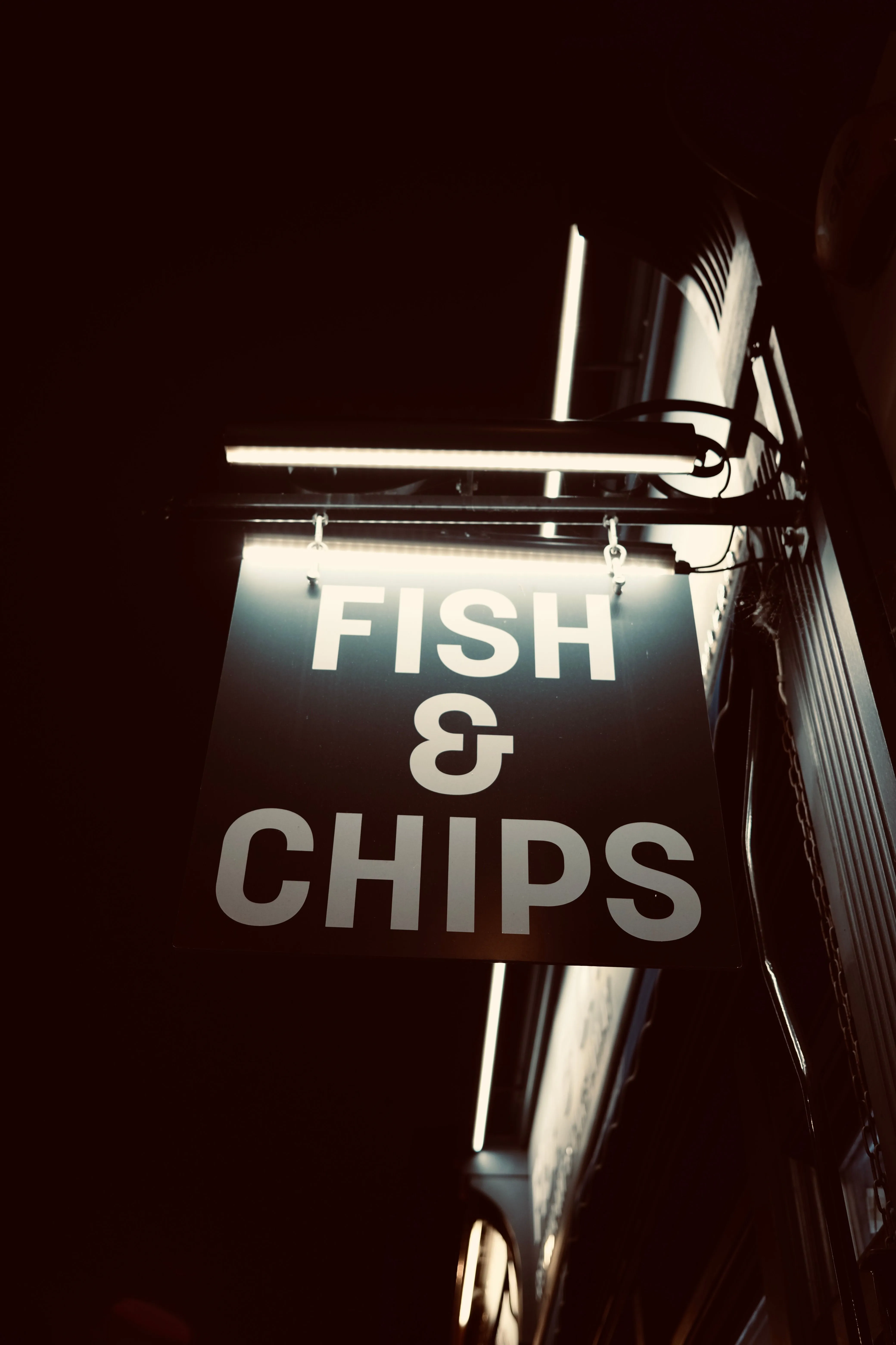 Illuminated hanging FISH & CHIPS shop sign at night