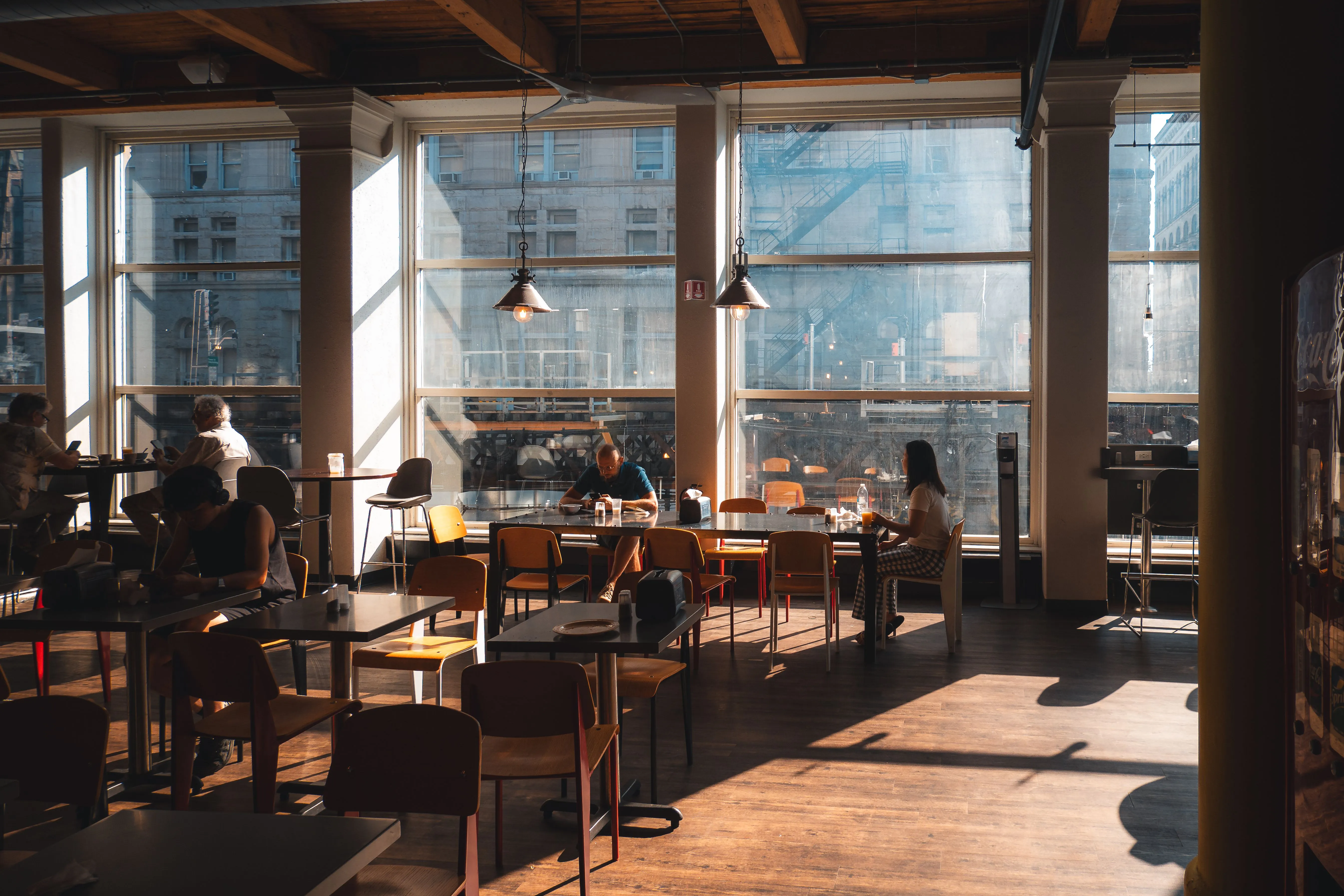 Sunlit loft-style cafe with diners at tables by large windows