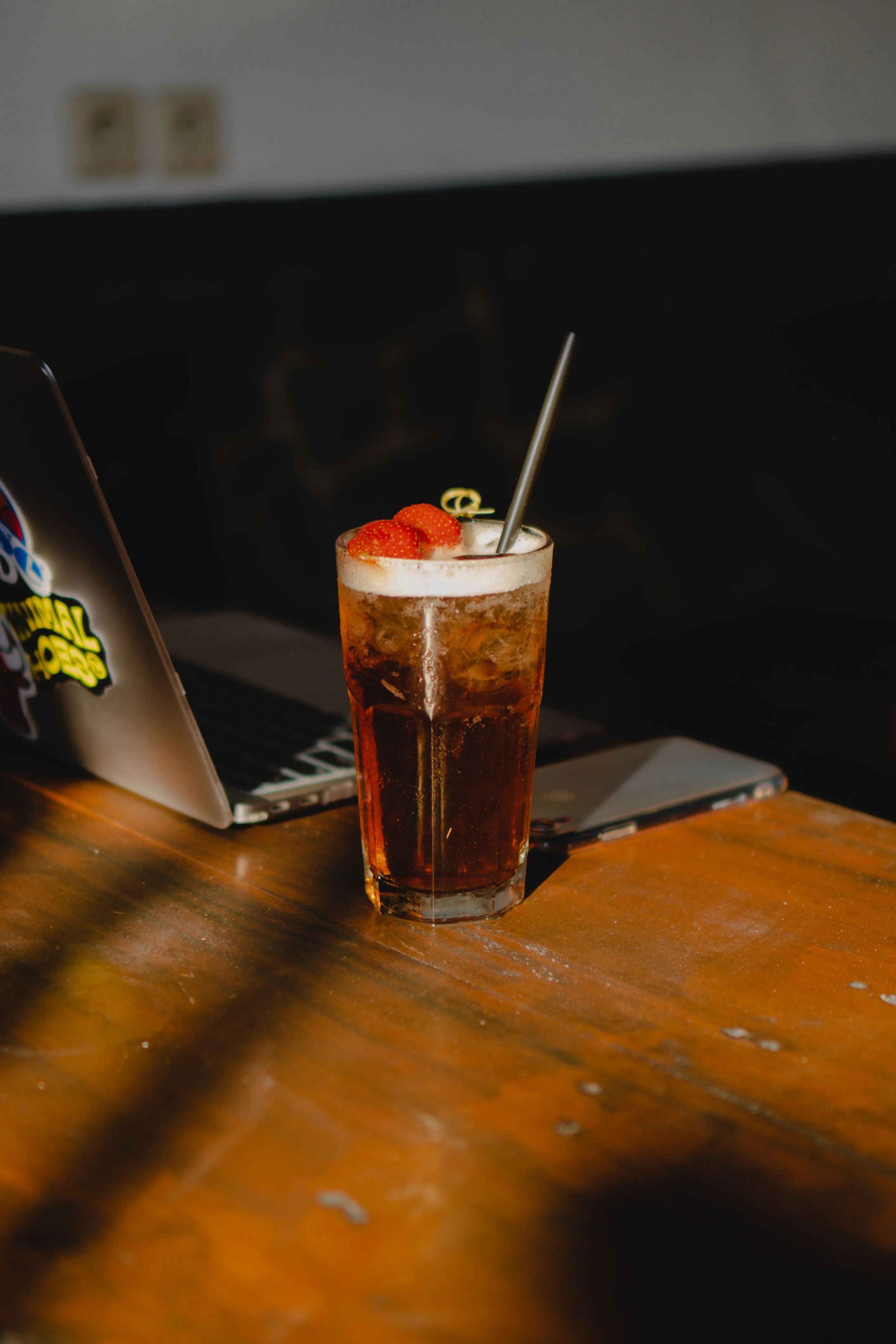 Iced drink with strawberries on wooden table beside laptop and phone